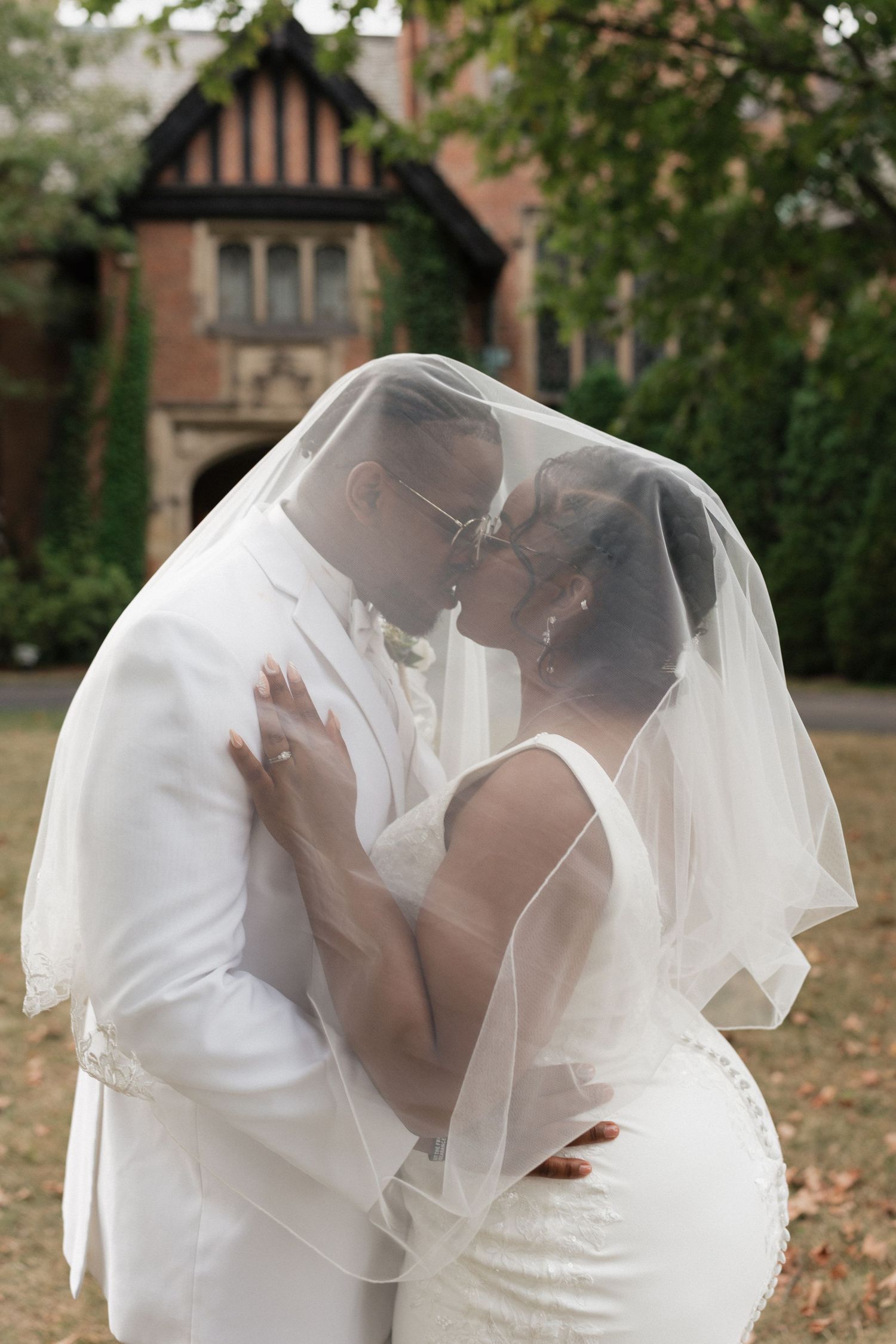 A romantic kiss under a flowing veil with Tudor-style mansion in background.