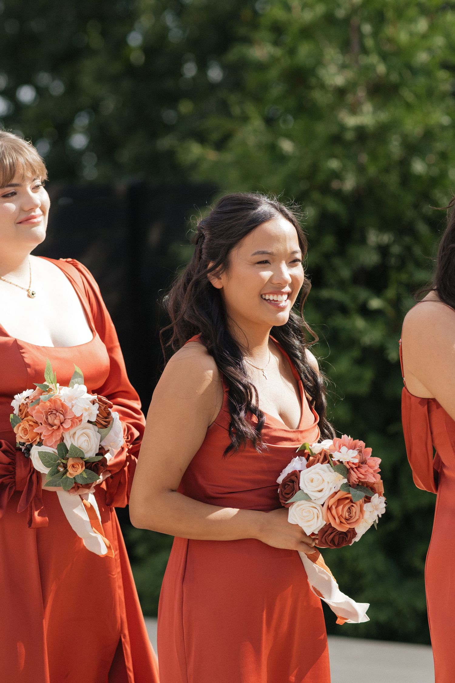 Bridesmaids in coral dresses holding peach and white floral bouquets.