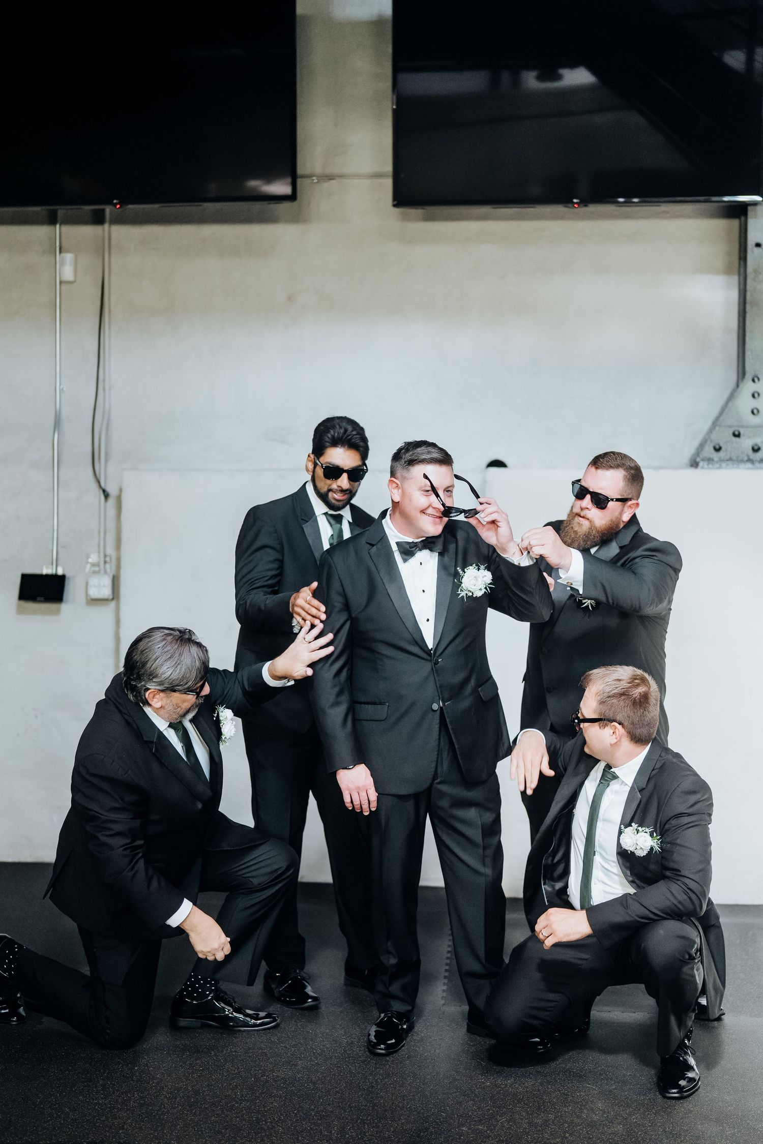 Groomsmen in black suits pose playfully in a creative sequence of photos against a white wall.