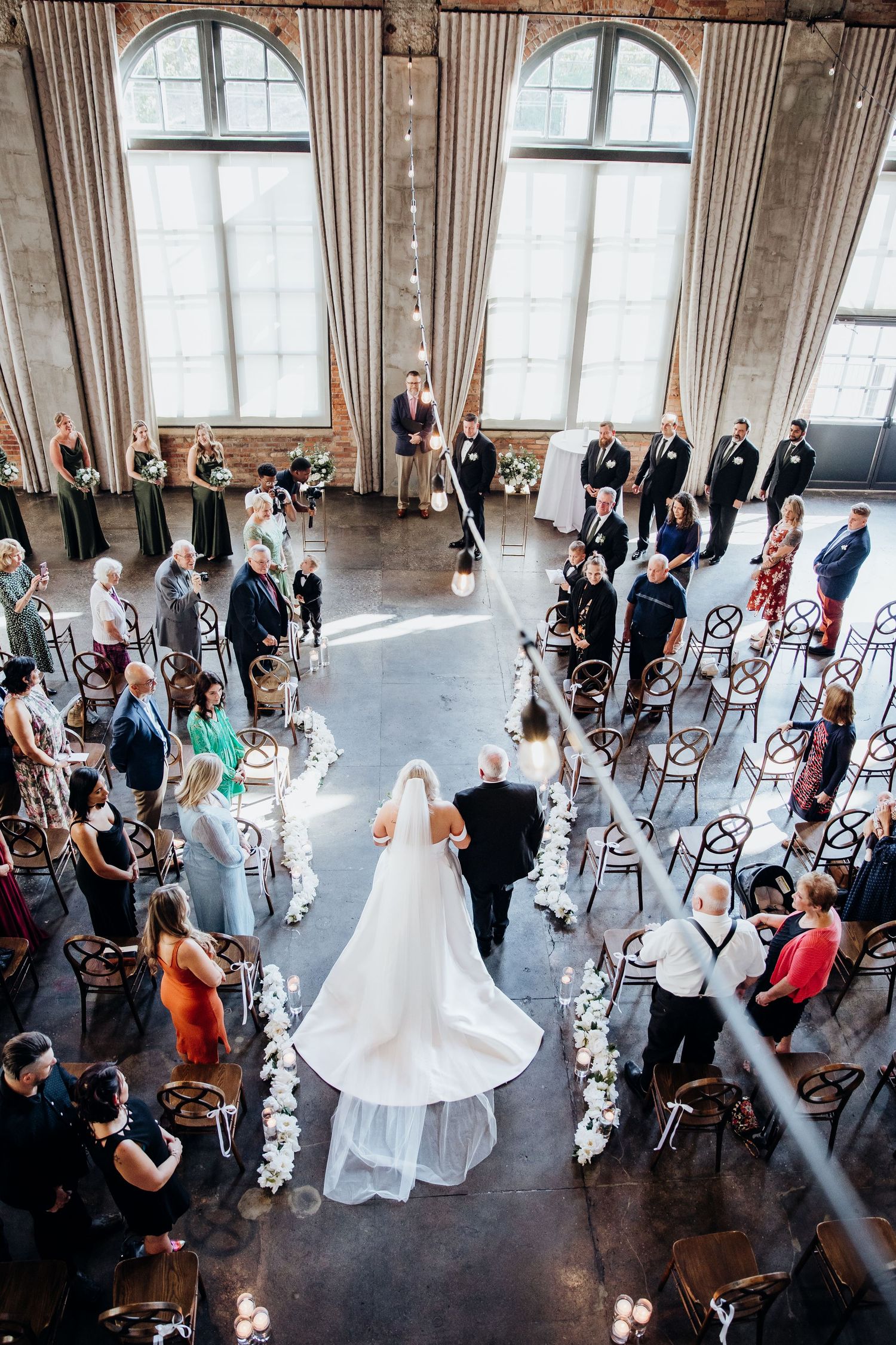 Overhead view of a wedding ceremony in an elegant venue with arched windows and guests lining both sides of the aisle.