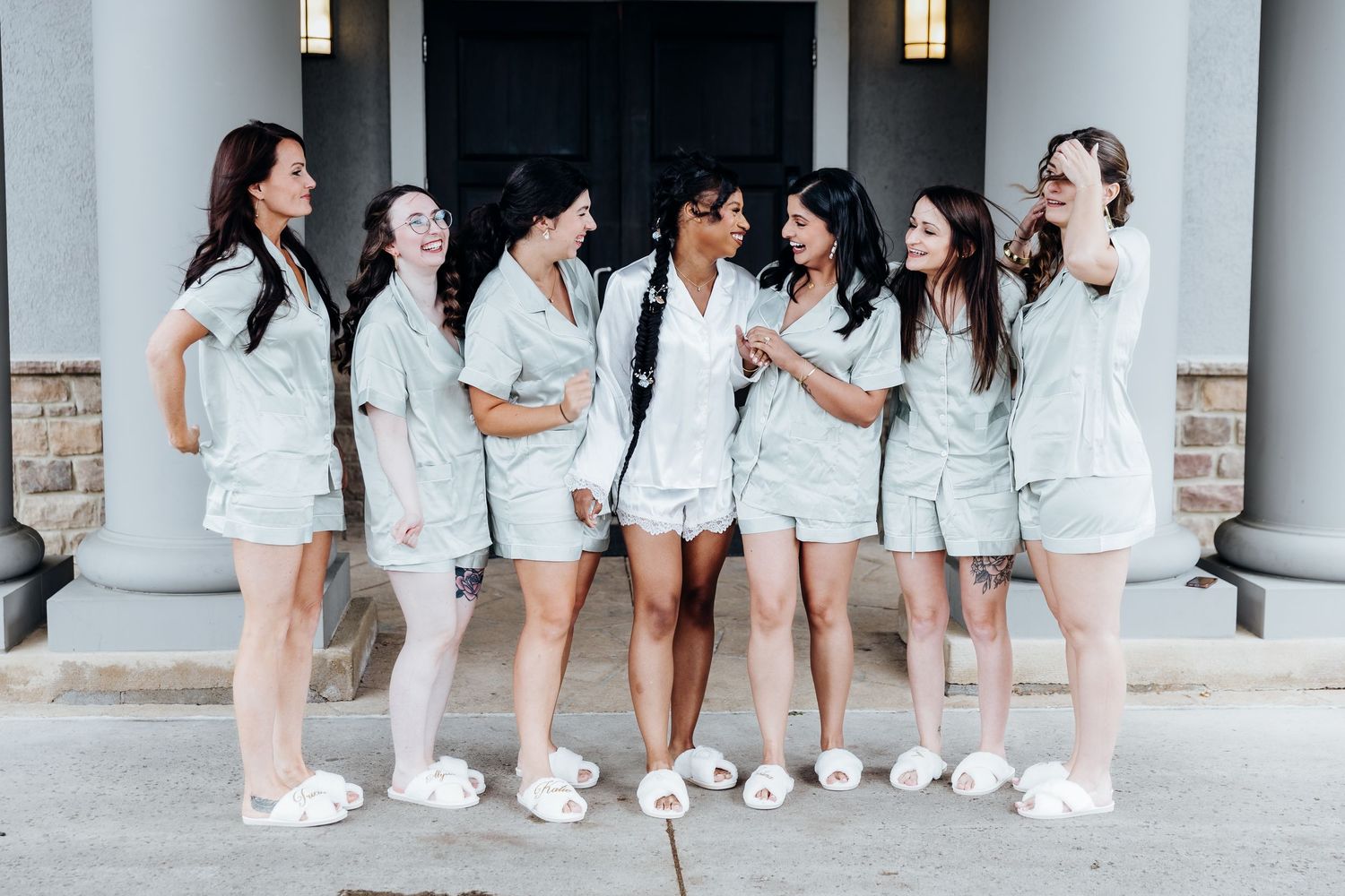 Bridesmaids in white robes sitting together on a porch with white columns.