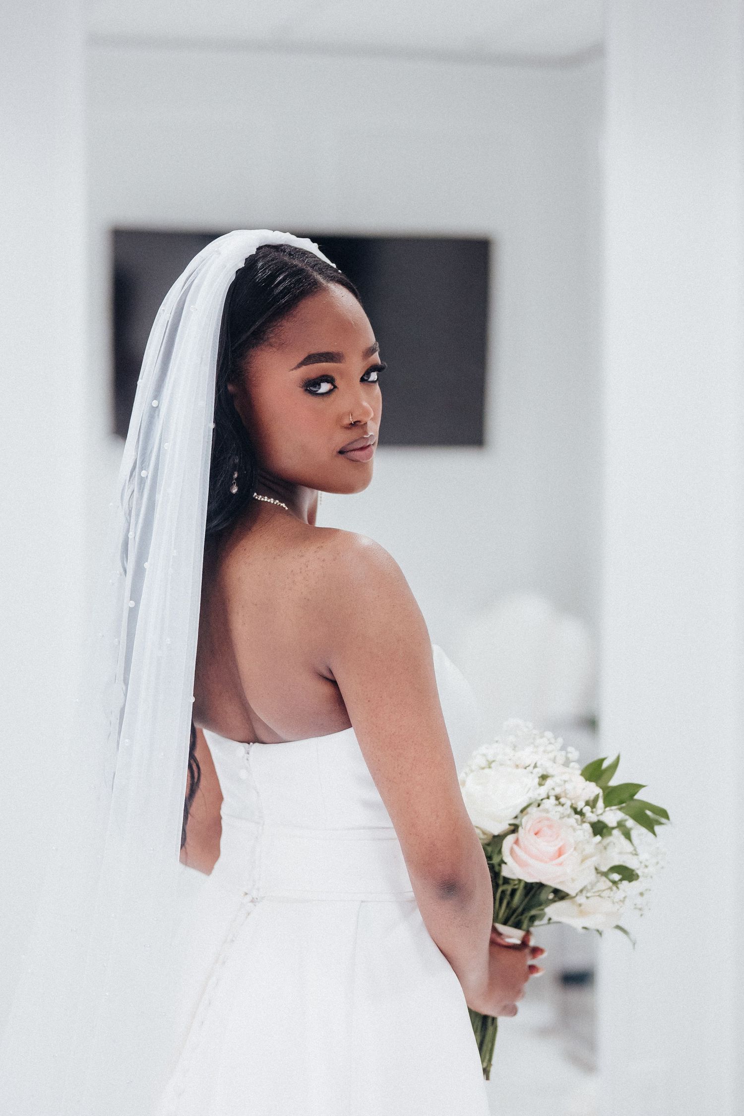 A bride in a white wedding dress holds a bouquet while looking over her shoulder in an elegant pose.