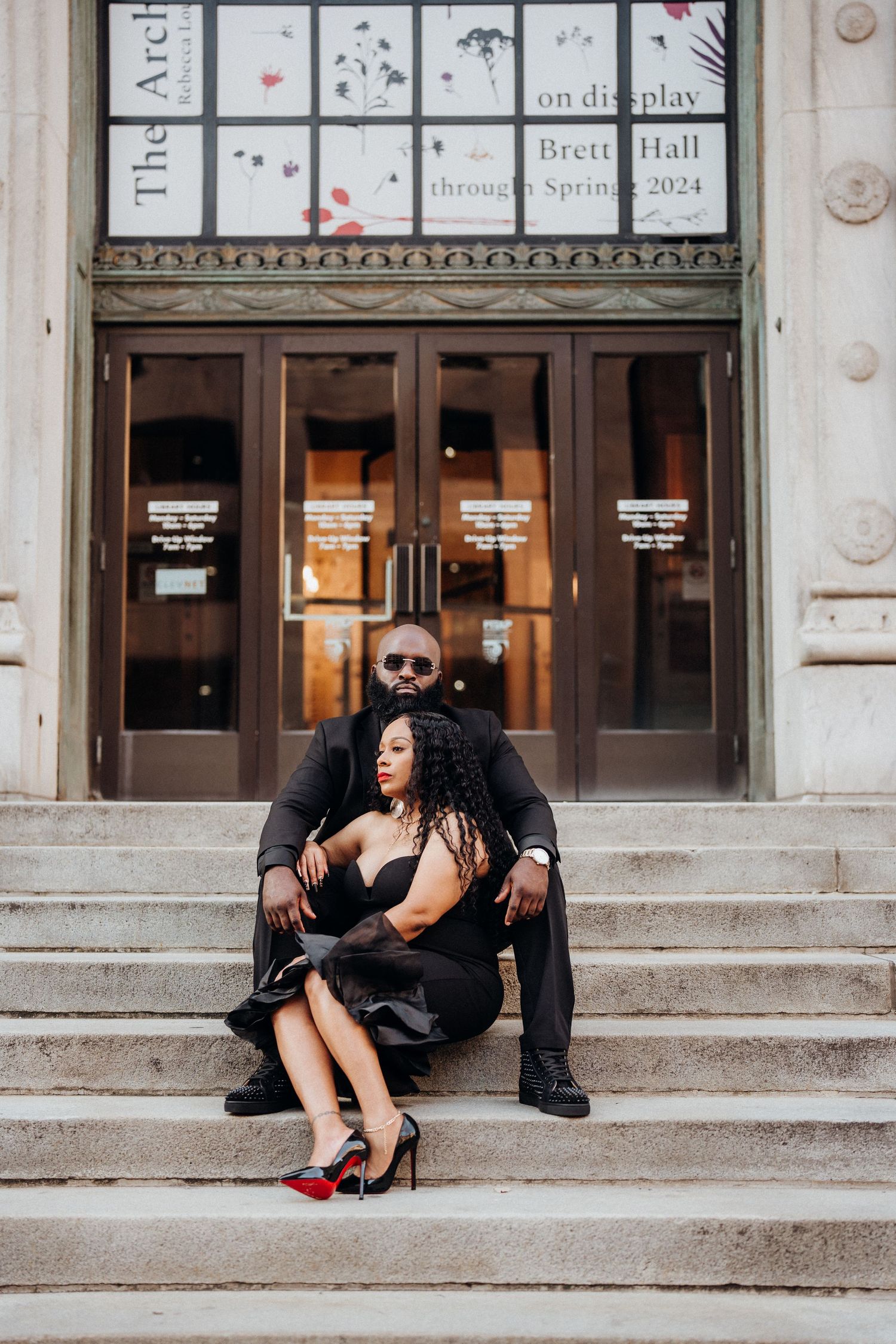Stylish couple posing on grand stone steps in front of historic building entrance.