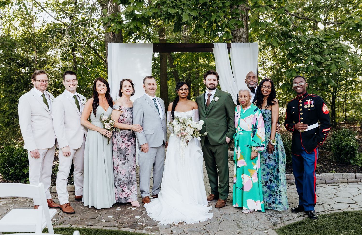 Wedding party poses together outdoors in pastel attire against a natural garden backdrop.