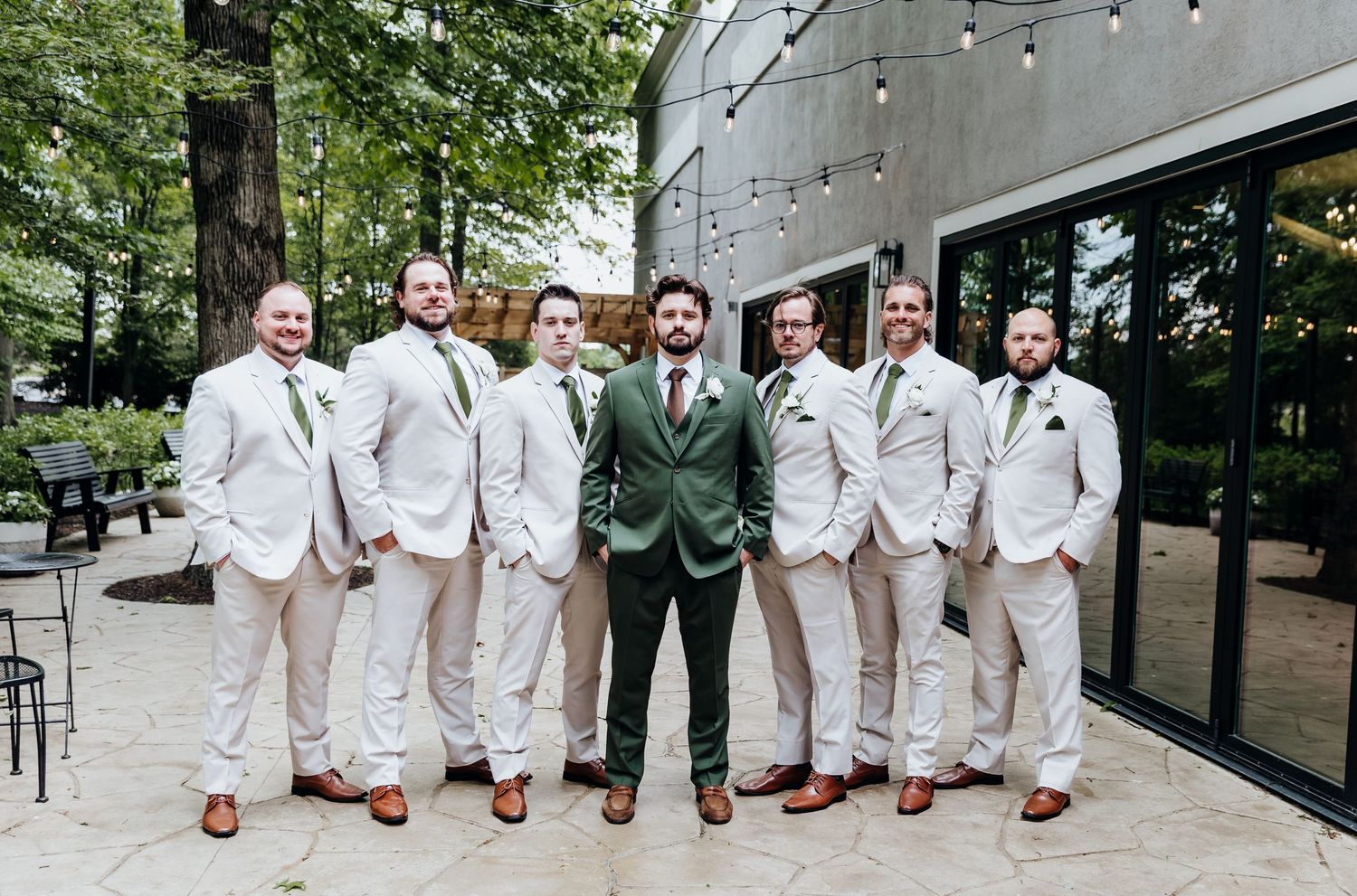Wedding party wearing light colored suits with red shoes pose together in front of a modern building.