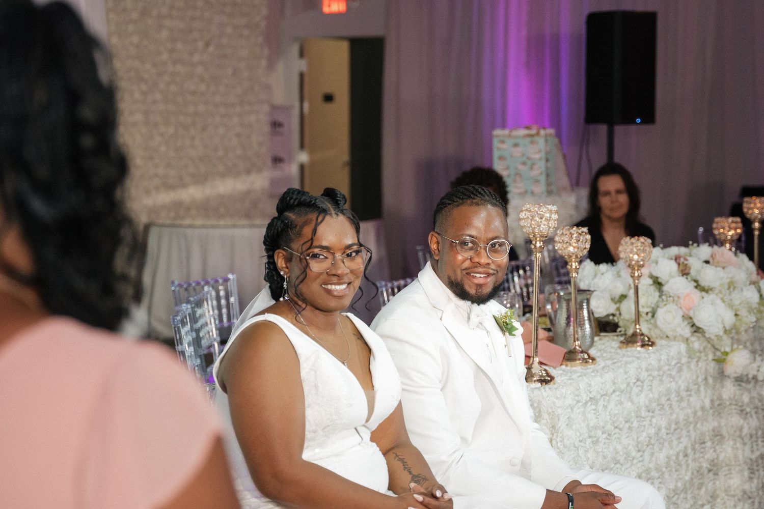 Wedding reception guests enjoying celebrations at decorated indoor venue with purple lighting.