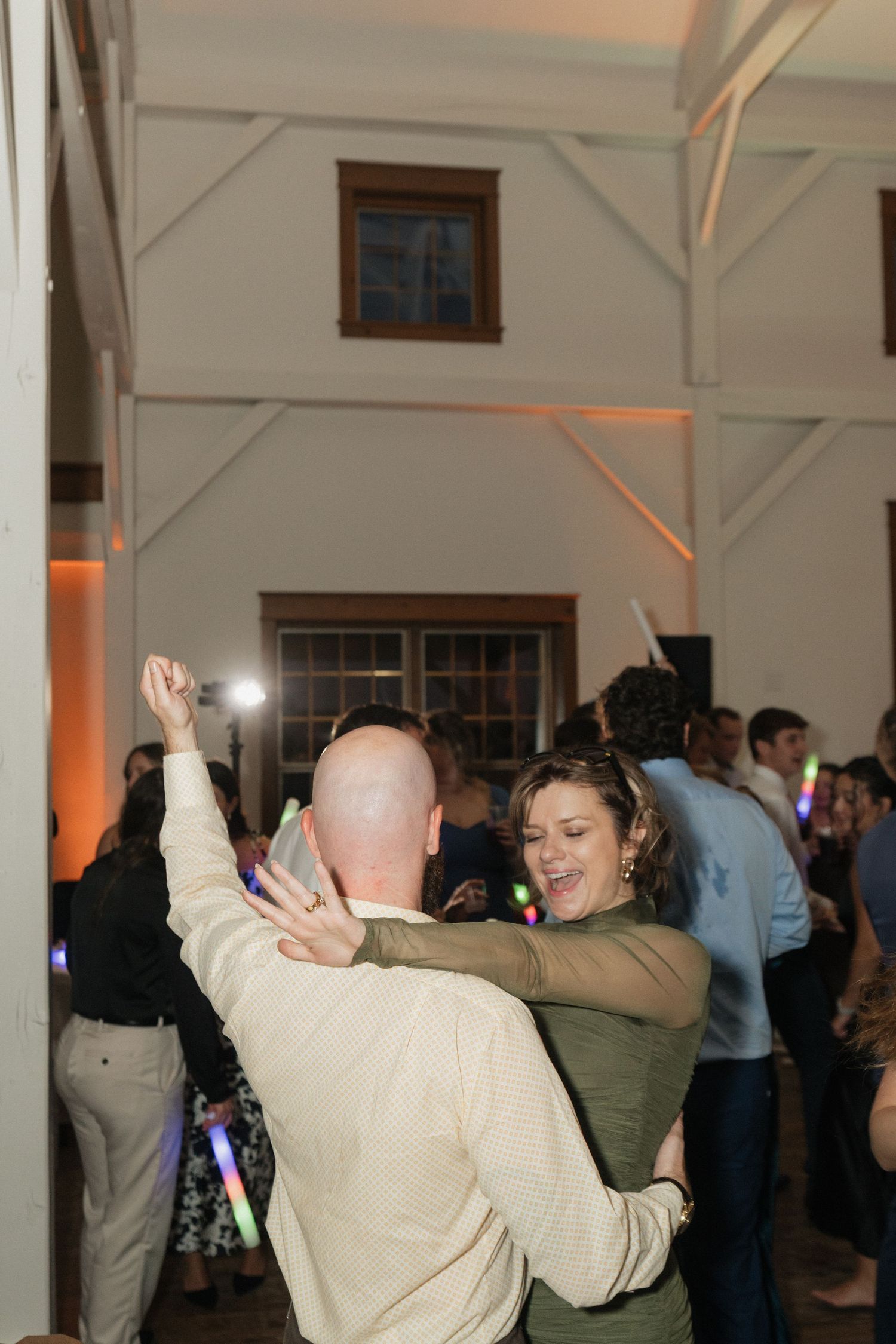 Wedding guests dancing and celebrating at indoor reception with ambient lighting.