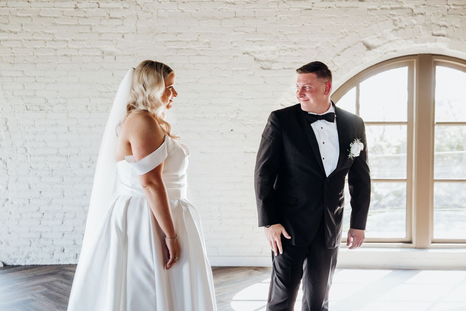 Wedding first look moment captured in a bright white brick room with natural lighting.