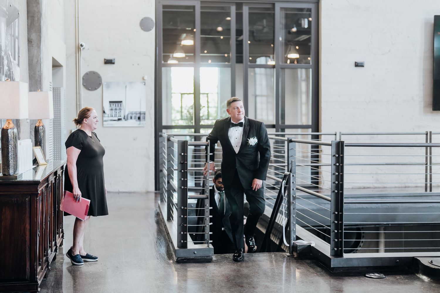 A wedding first look sequence in a bright modern venue with white walls and black railings.
