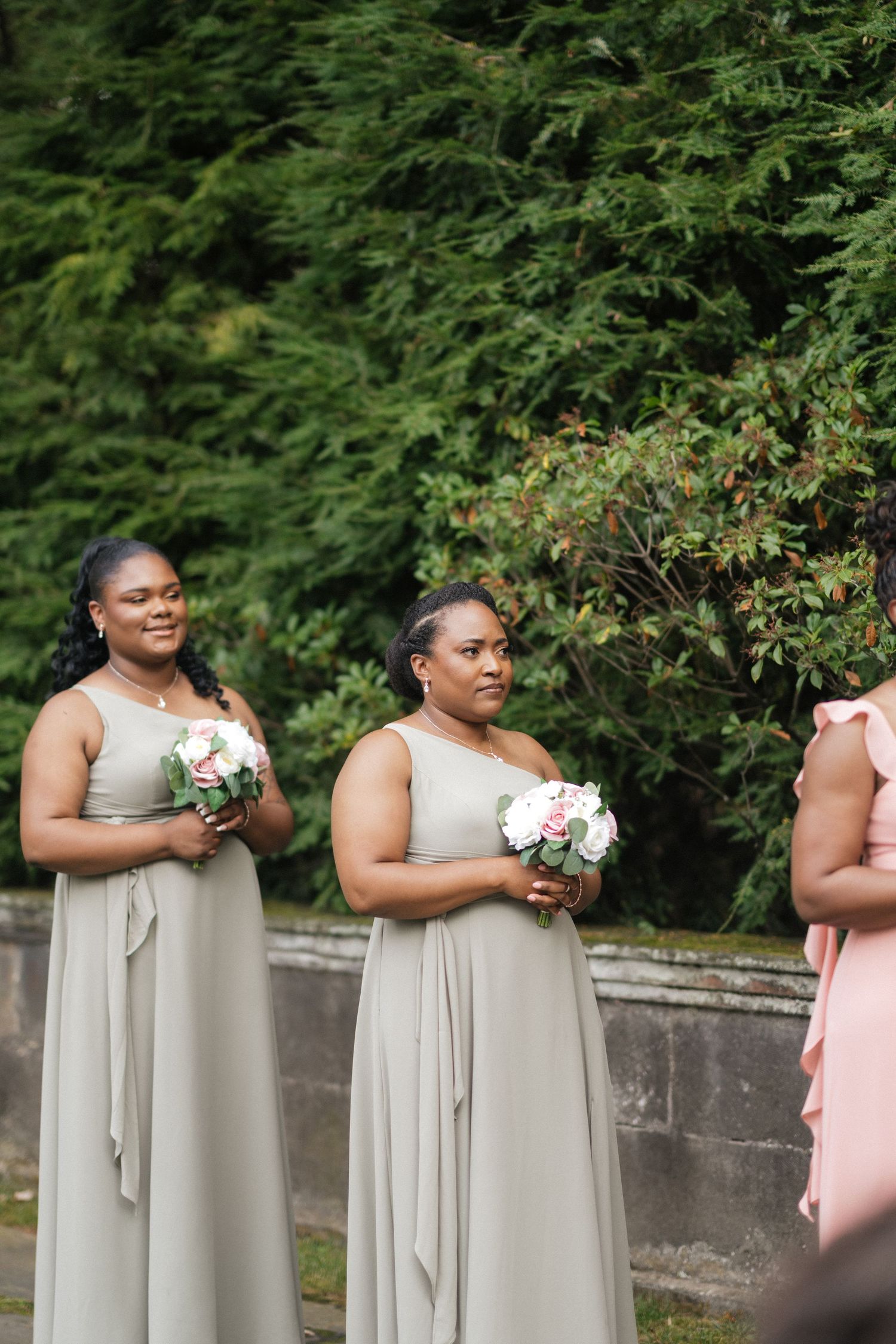 Bridesmaids in elegant gray dresses hold white bouquets in garden setting.