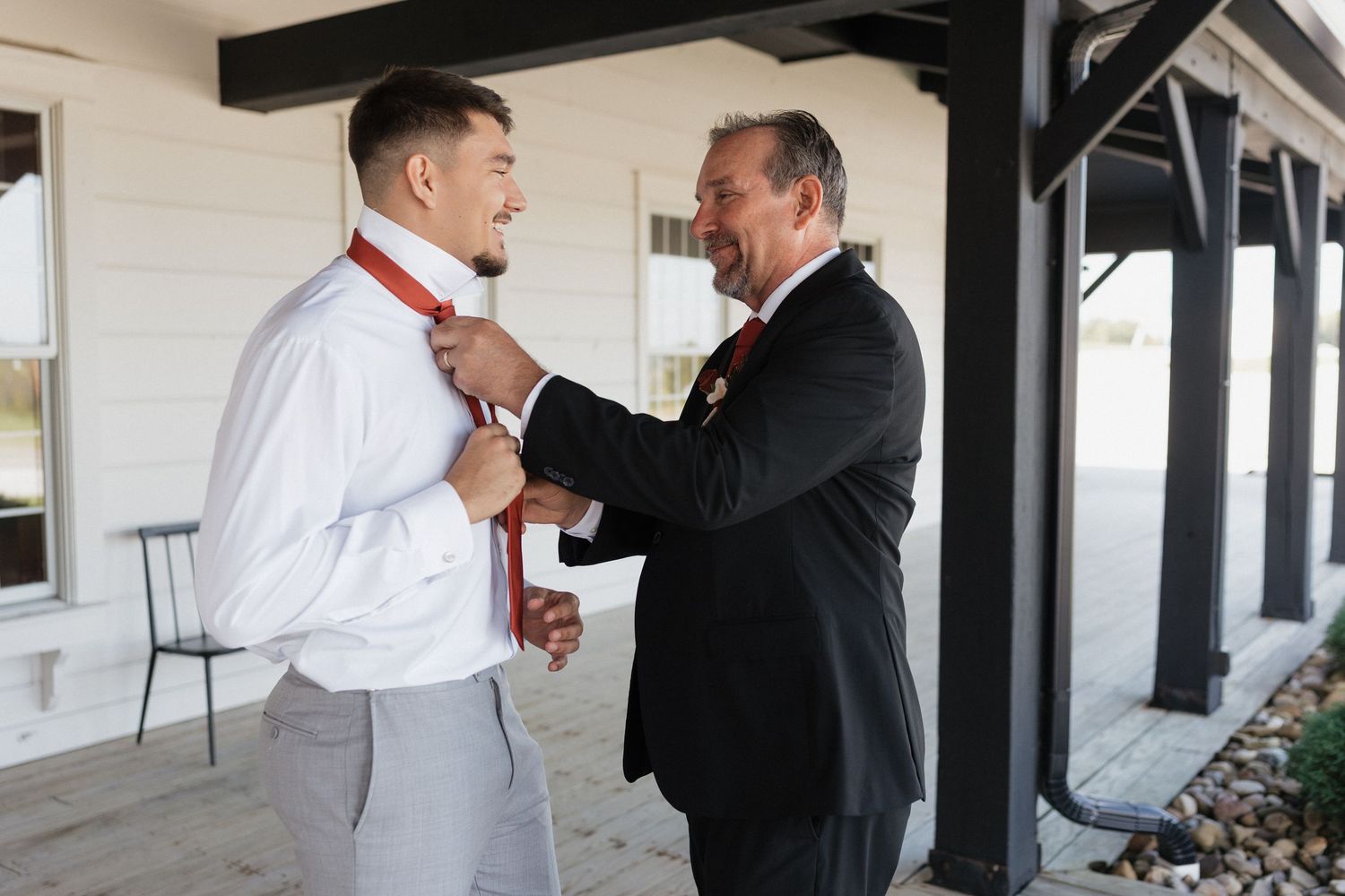 A formal moment between two people adjusting a red tie before a special occasion.