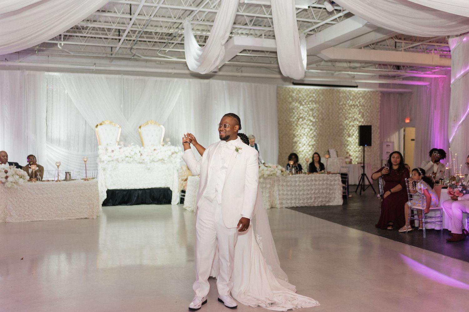 Wedding reception celebration in a modern white venue with purple accent lighting.
