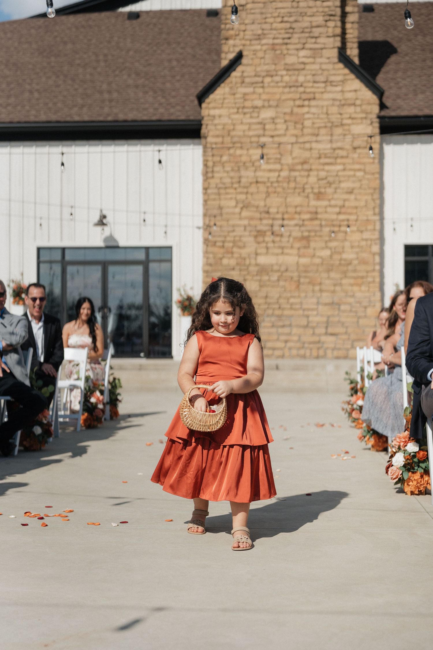 Wedding party members in rust-colored dresses walking on a stone patio outside a venue.