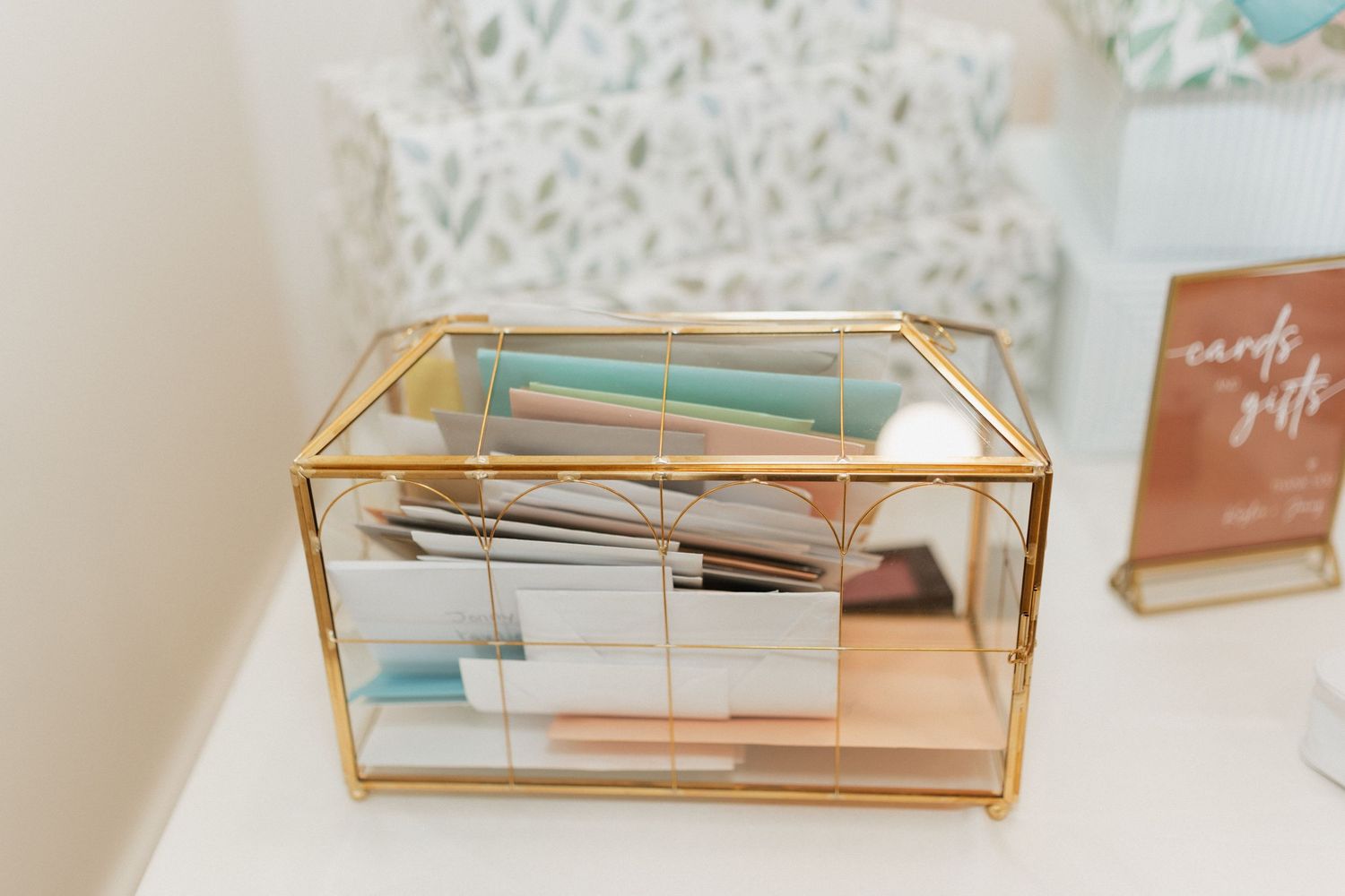 A gold glass display box containing wedding stationery and keepsakes.