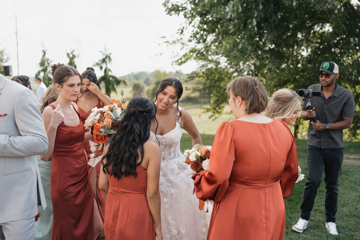 Wedding party members in rust-colored dresses gather outdoors for photos.