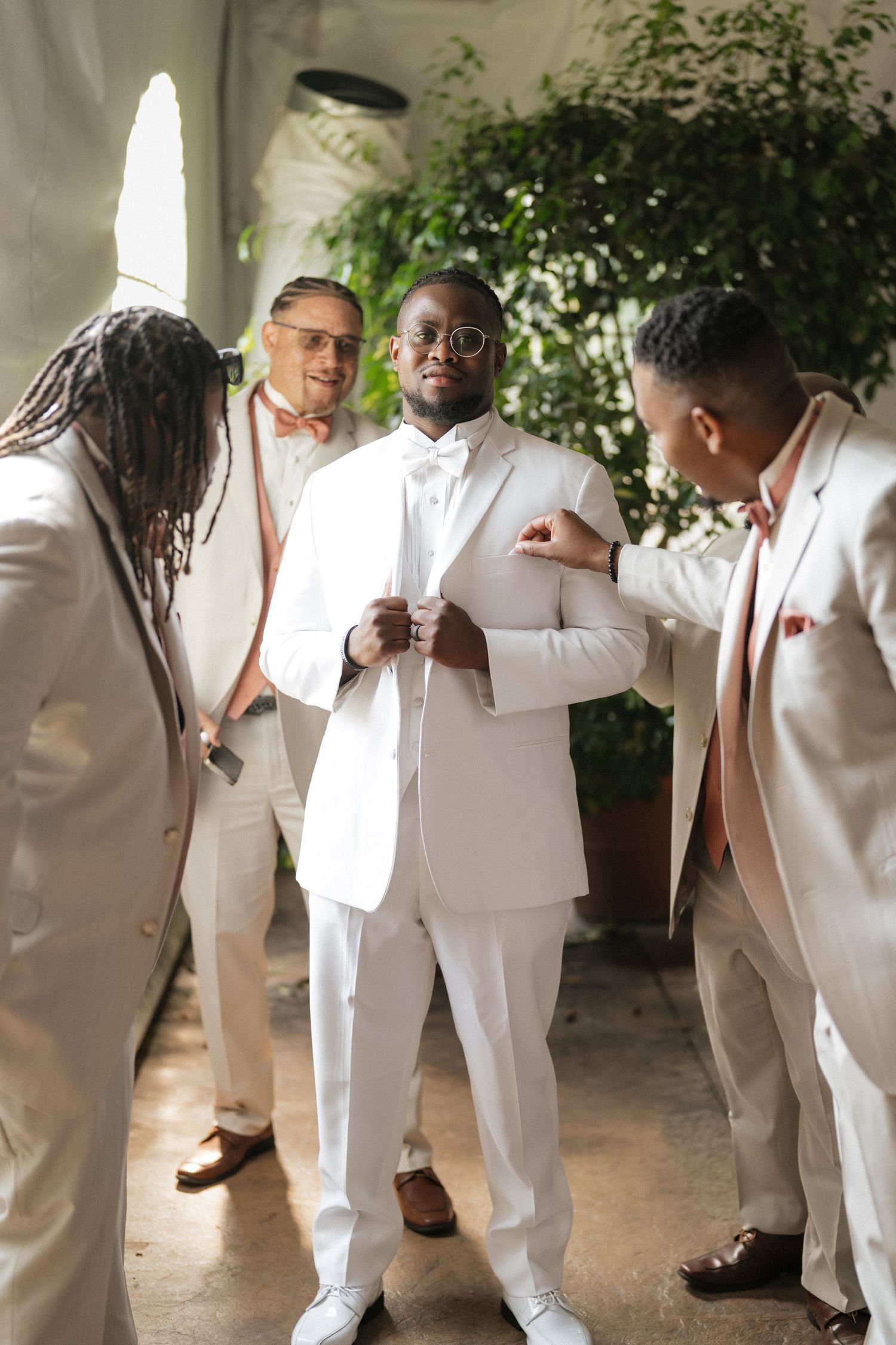 Groomsmen in crisp white suits share a lighthearted moment together during wedding preparations.