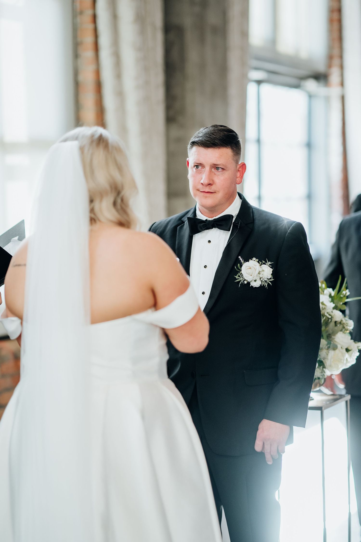 A first look moment between a bride in white and groom in black tuxedo in an elegant indoor setting.