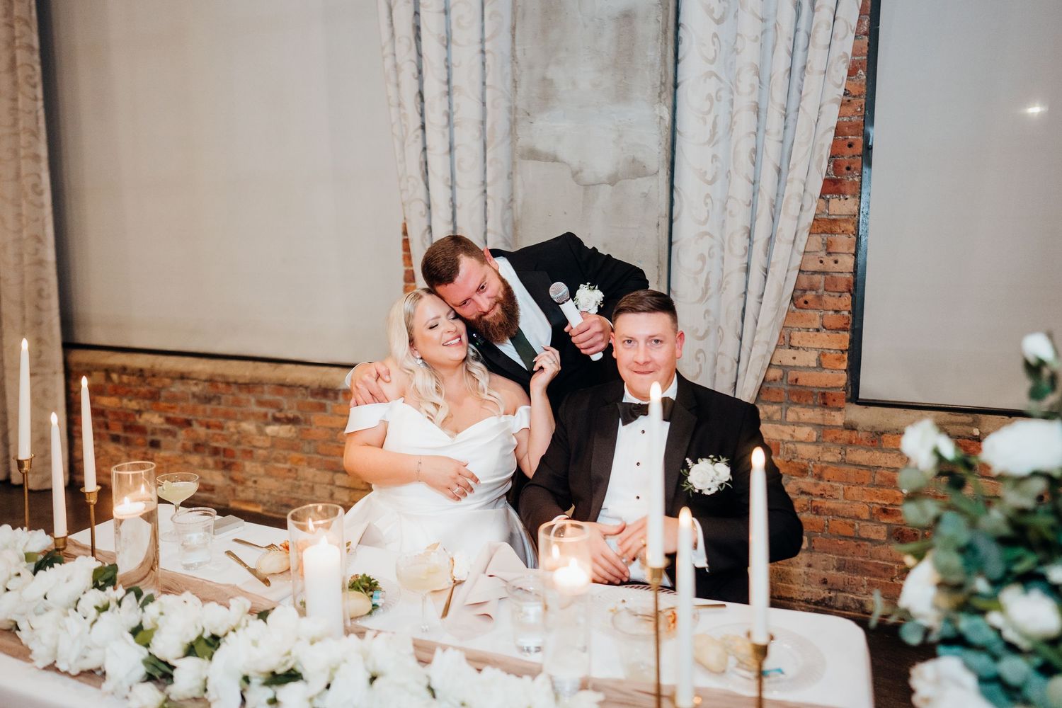 Wedding celebration in an elegant brick-walled venue with floral decorations.