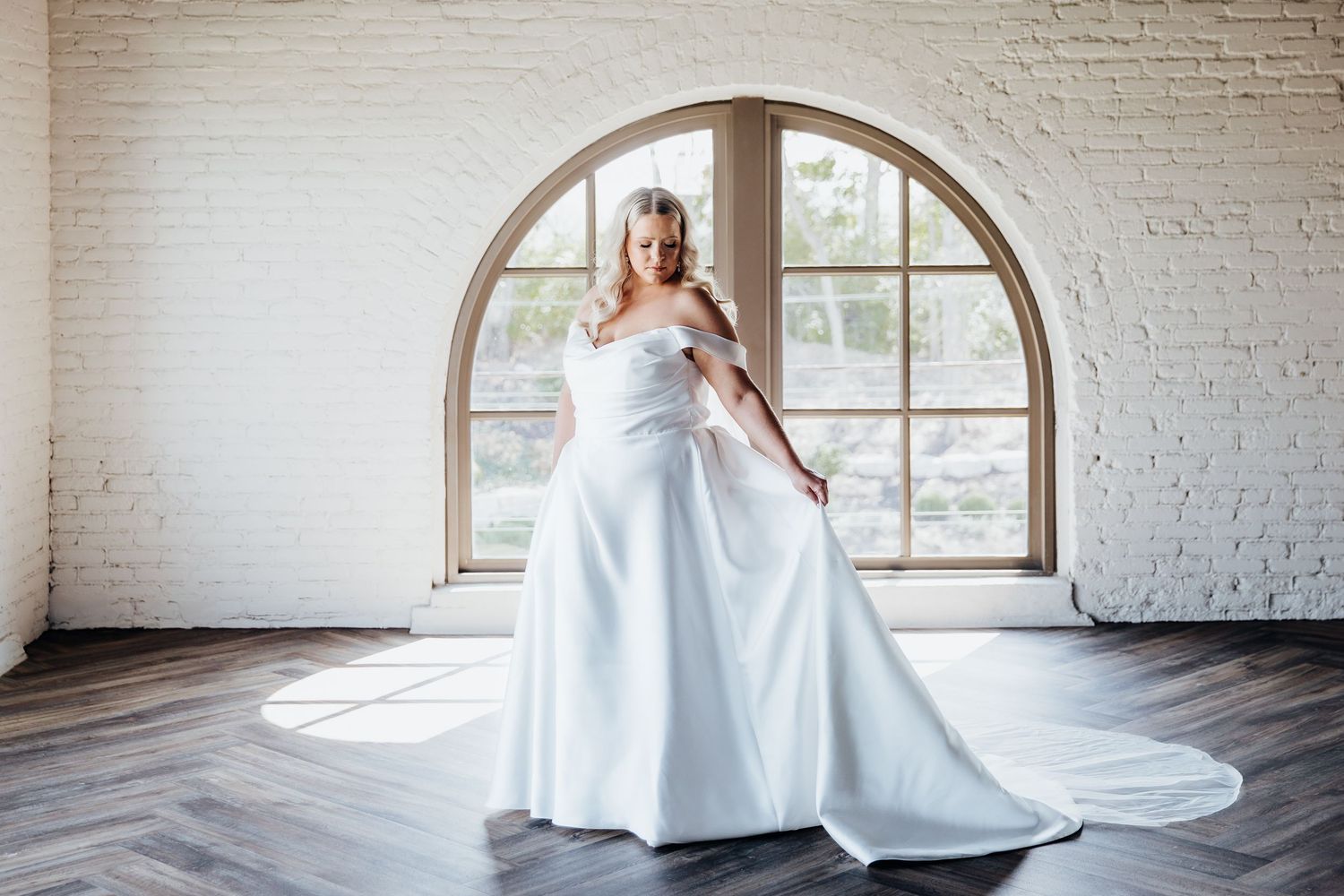Bride in flowing white gown posing gracefully in front of arched windows.