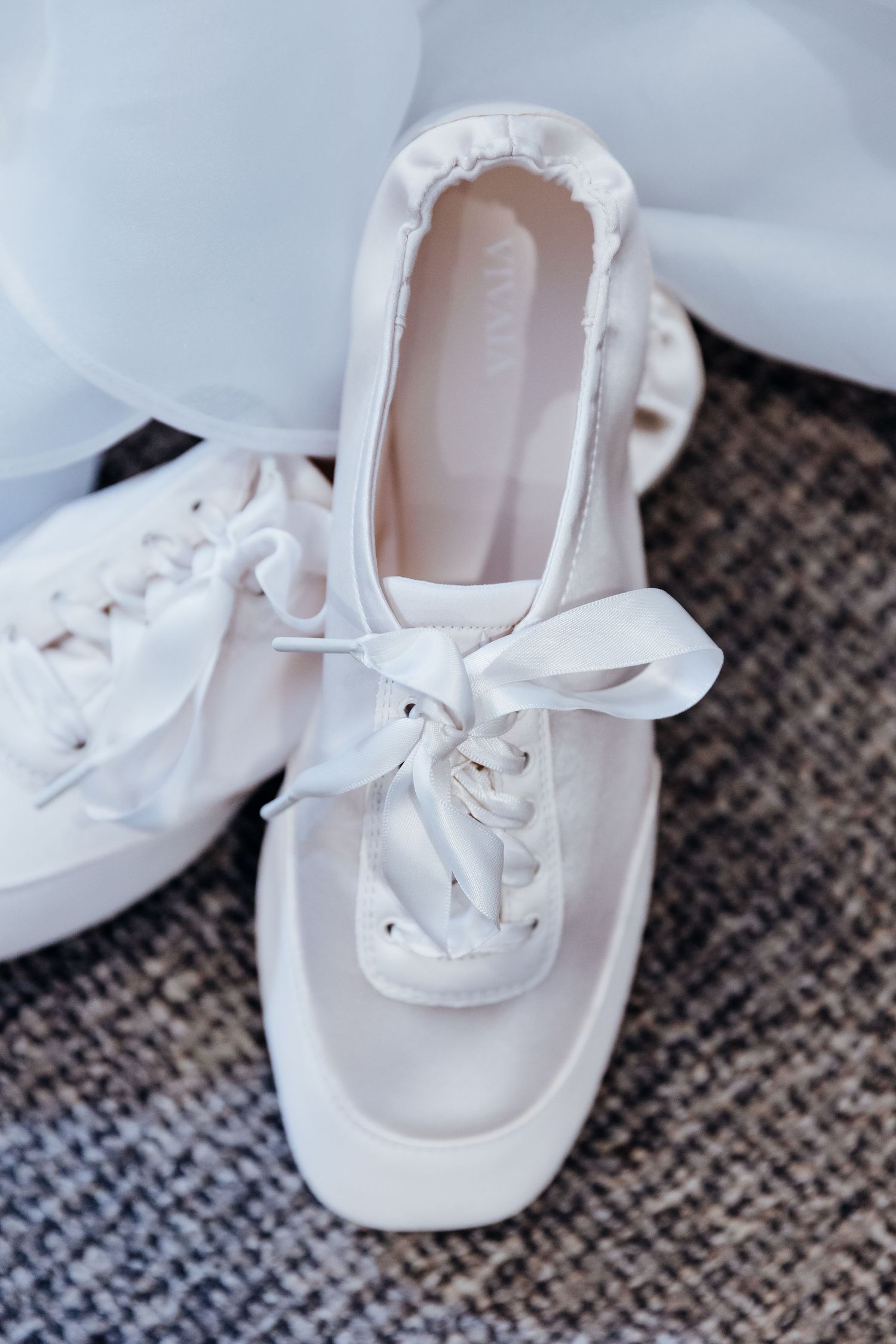White canvas sneakers with ribbon laces sit on a gray textured surface.