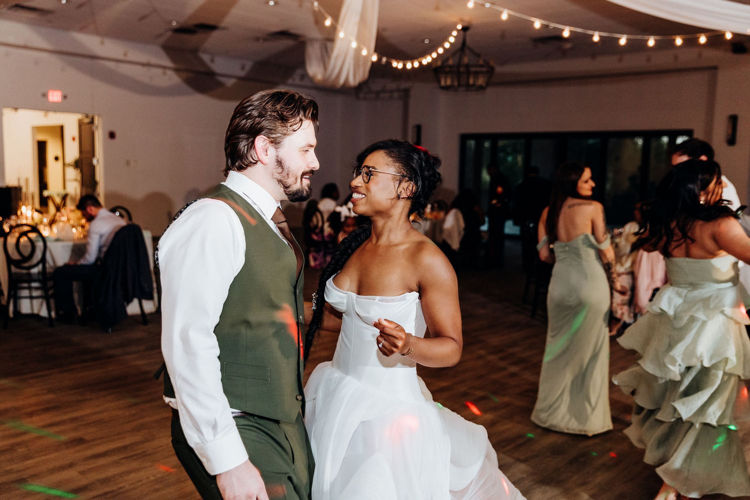 Newlyweds share a joyful moment dancing together at their wedding reception under string lights.