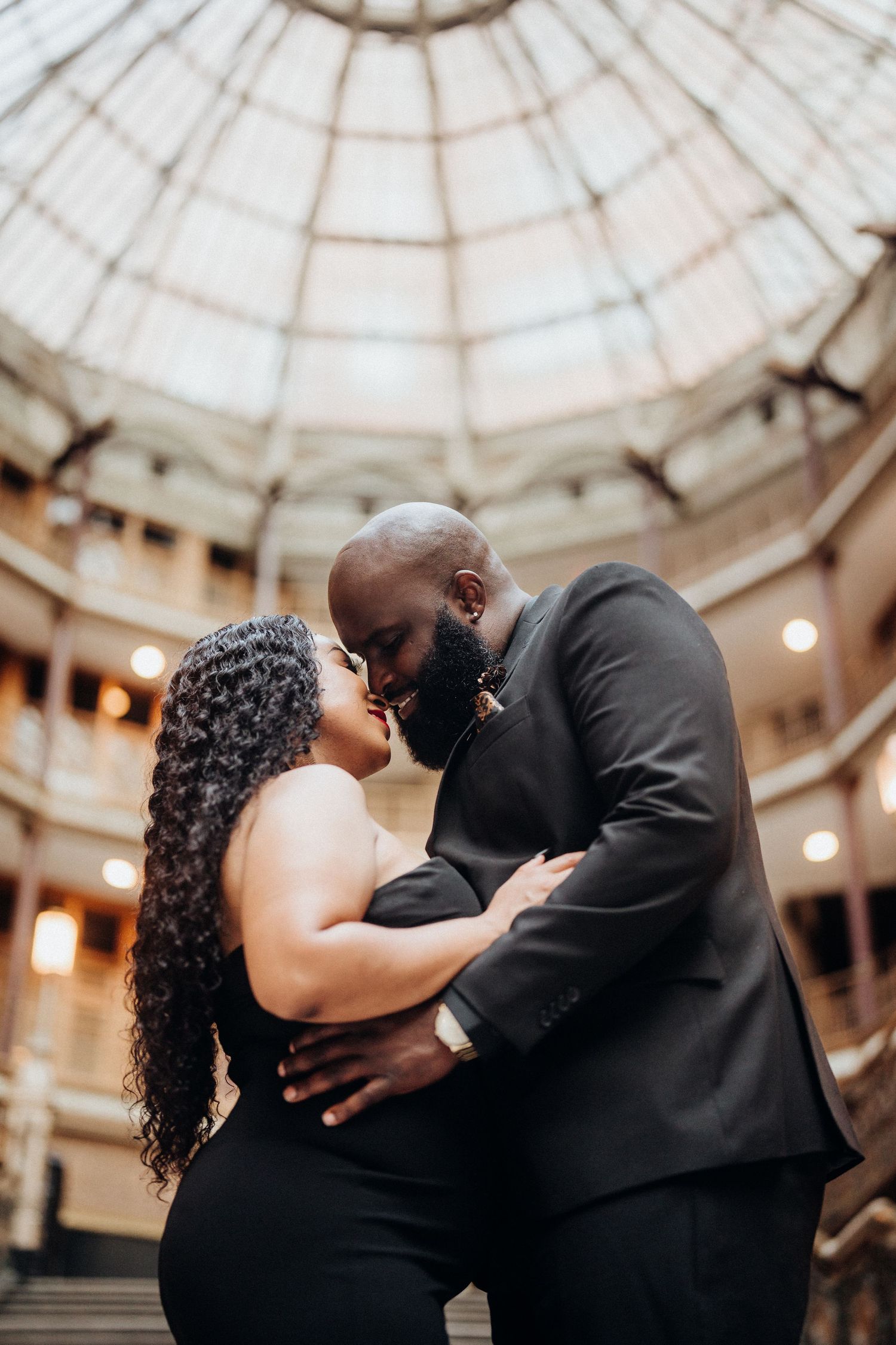 A couple embraces under a stunning domed ceiling in formal wear.