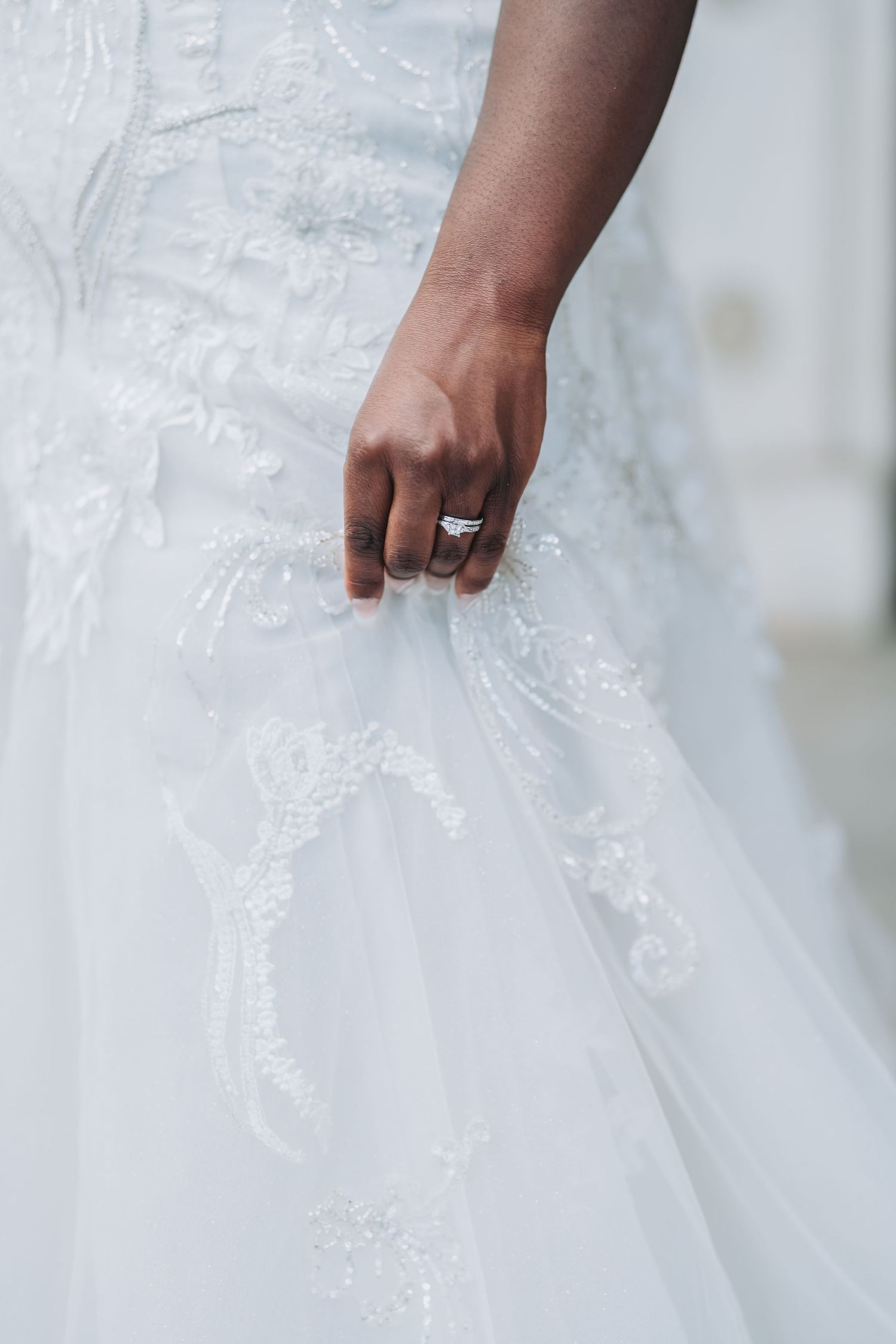Close up of a hand wearing an engagement ring holding a white lace wedding dress fabric.