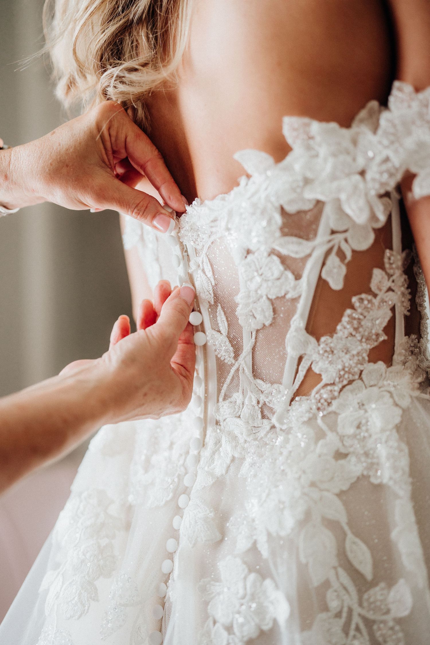 Close-up detail of intricate lace appliques being fastened on a wedding dress.