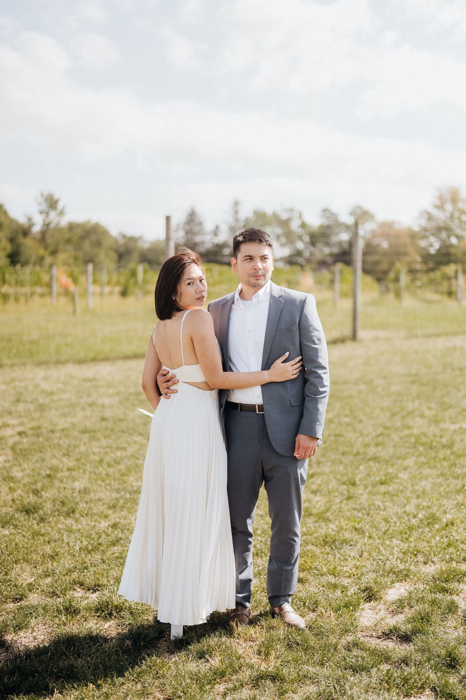A couple poses together in wedding attire against a pastoral background.