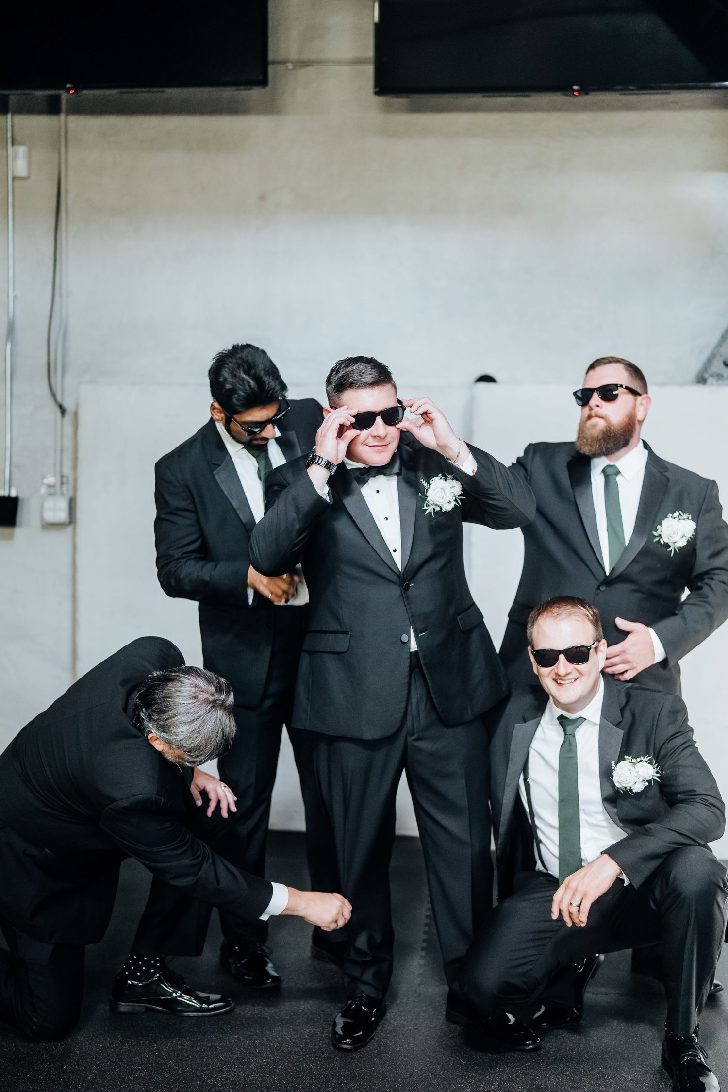 Groomsmen in black suits and sunglasses strike fun poses in a wedding photo shoot.
