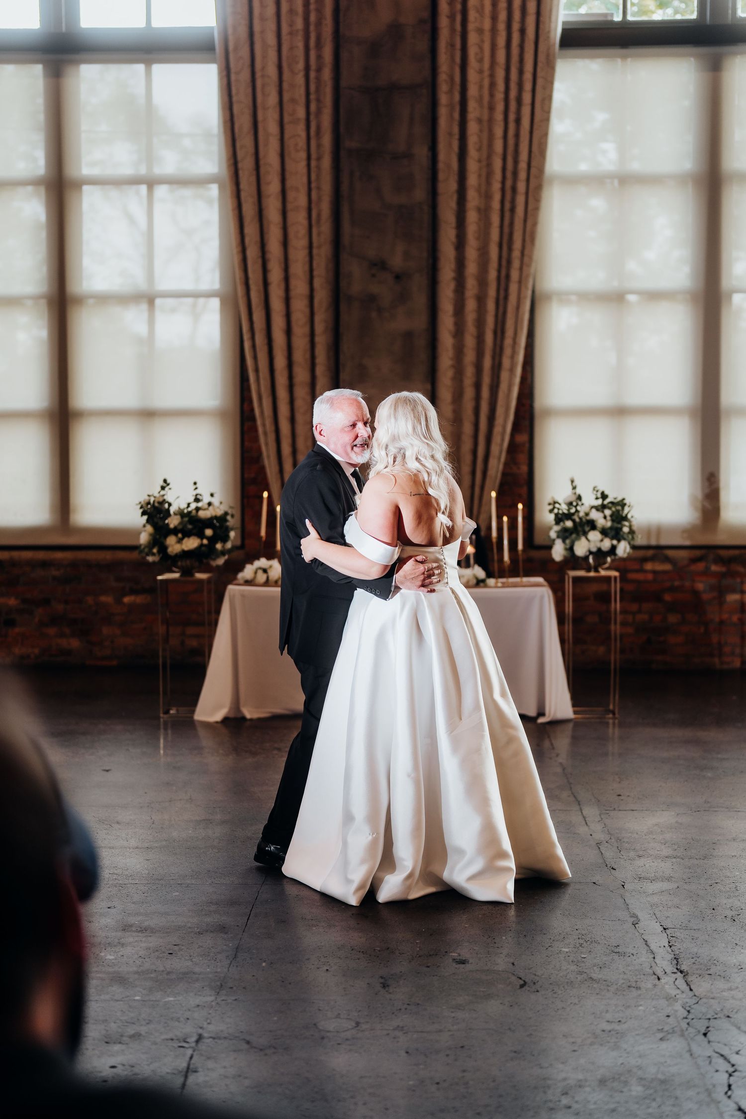 Romantic first dance moment in an elegant venue with large windows and draped curtains.