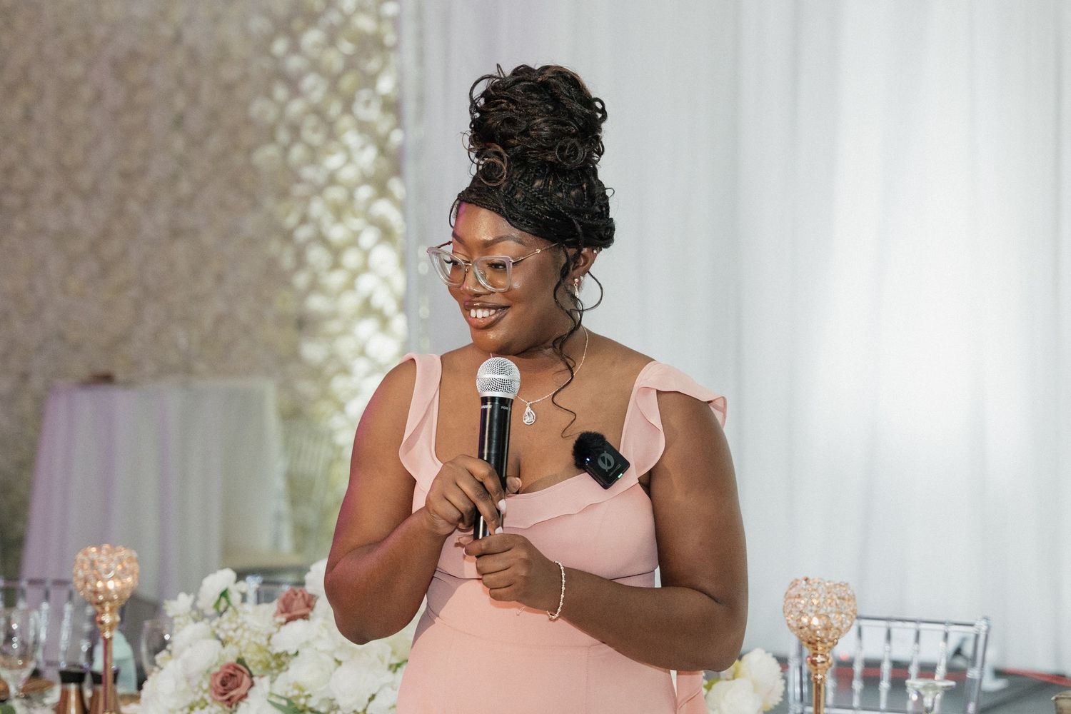 A person in a pink dress gives a speech at an elegant wedding reception.