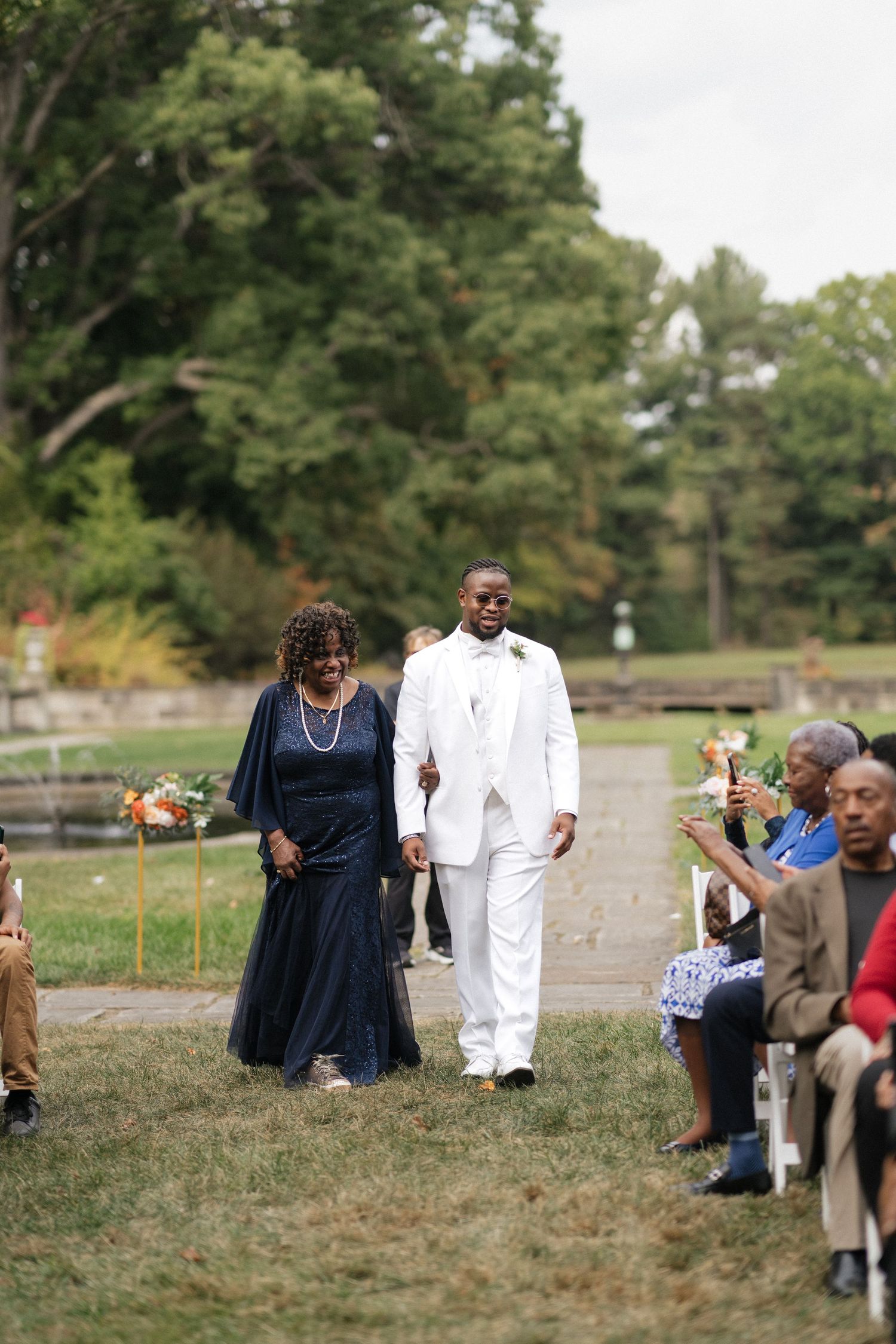 Wedding party members walk across a grassy outdoor venue path.