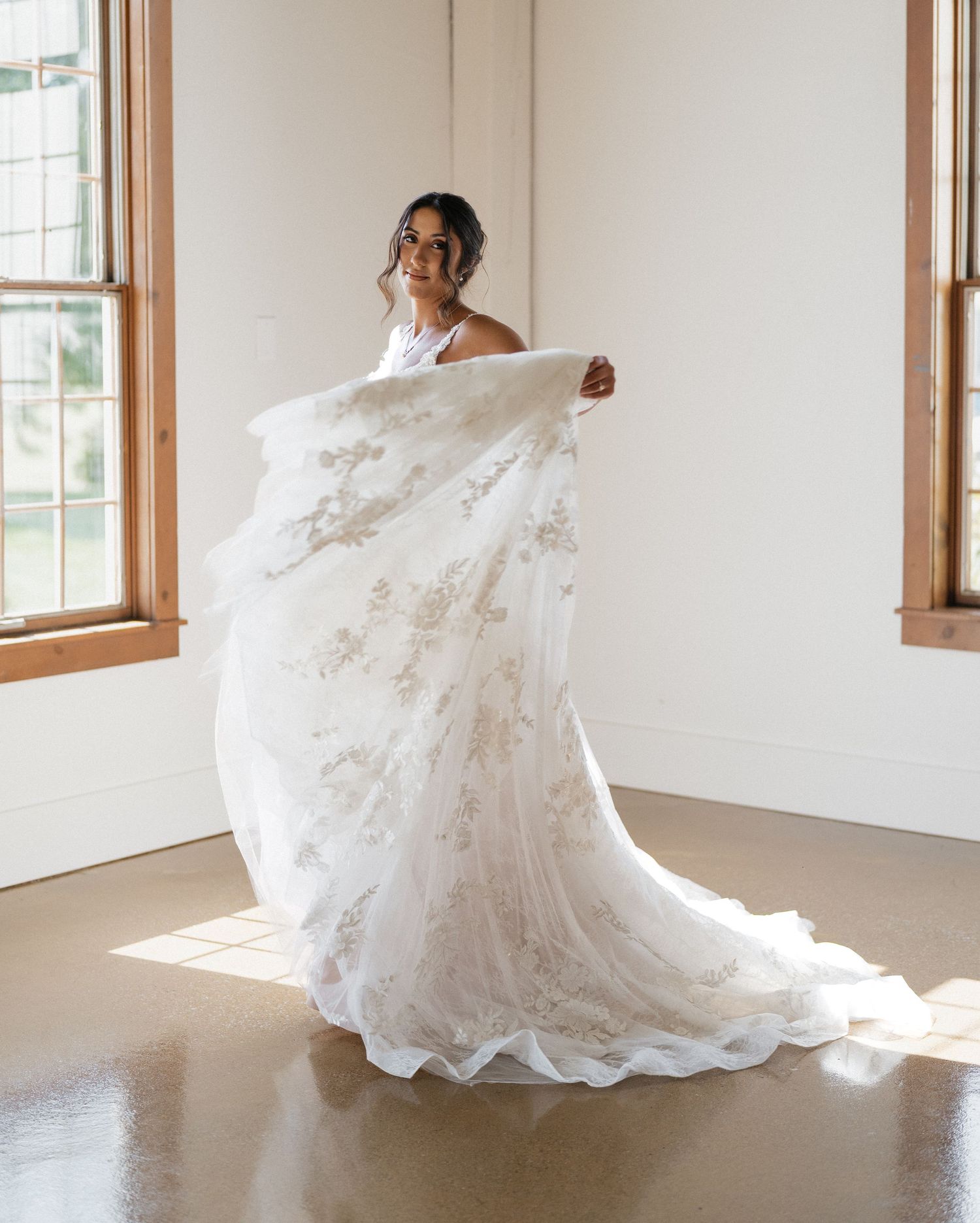 A flowing white lace wedding dress with train captured in natural window light.