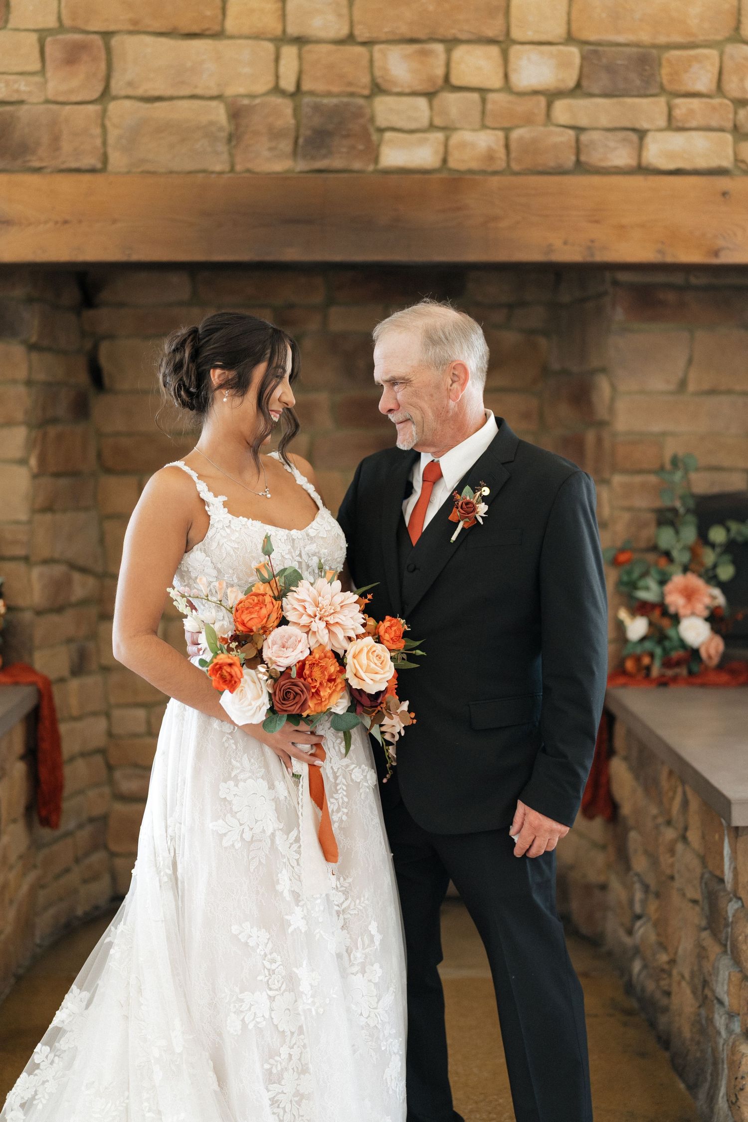 Elegant wedding portrait against stone wall backdrop with coral and white floral bouquet.