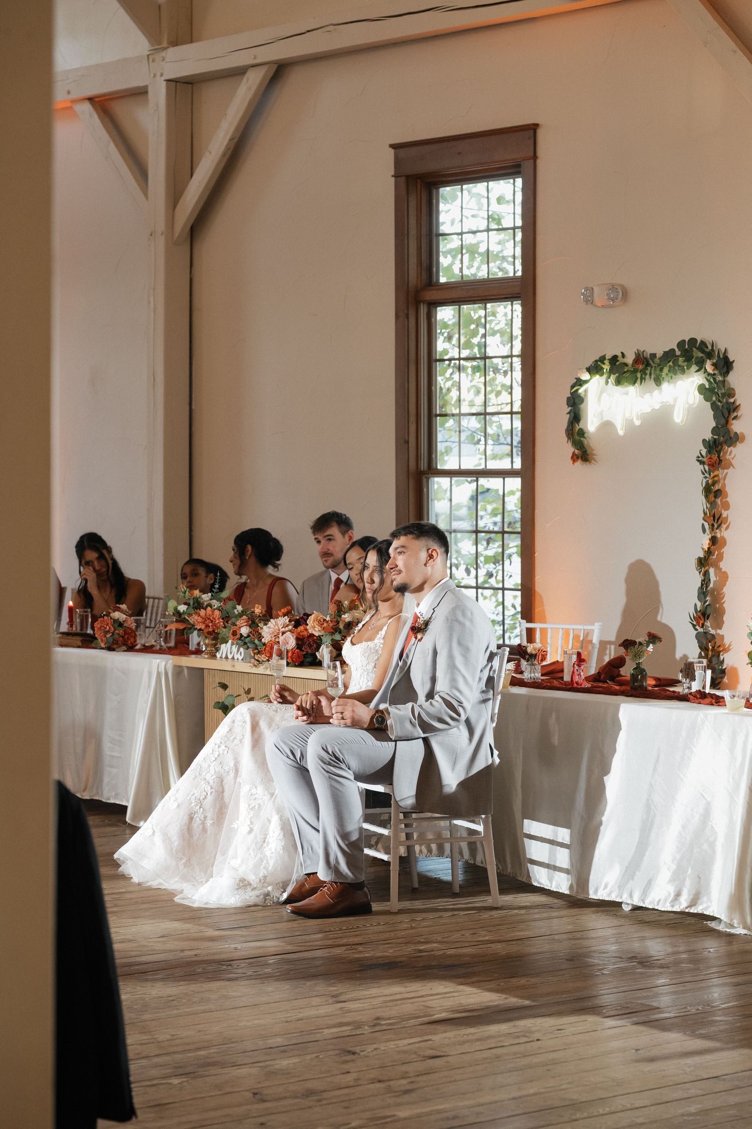 Light-filled reception venue with white-covered tables and rustic wooden floors.