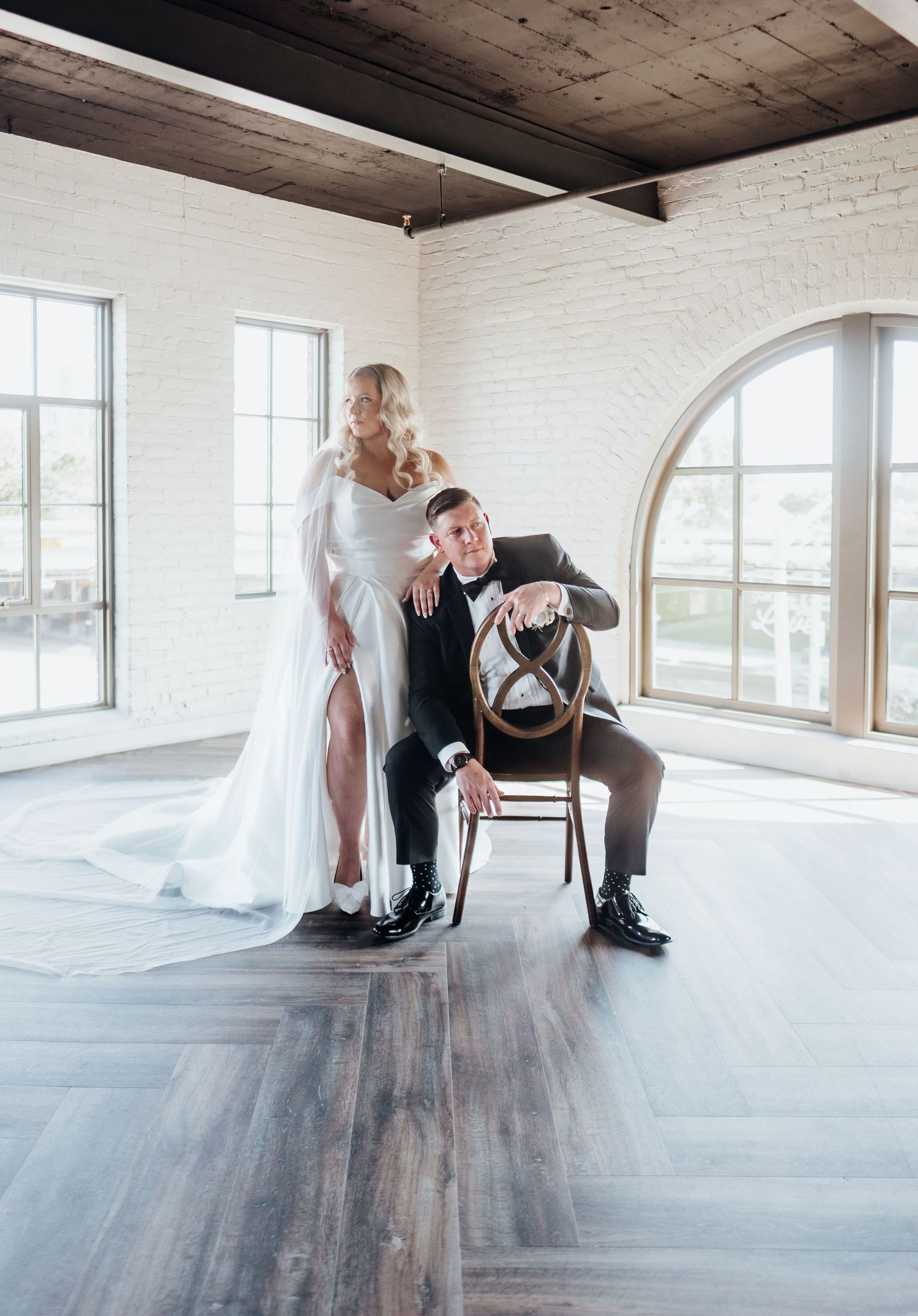 Creative wedding portrait in industrial venue with bride and groom posing with chair.