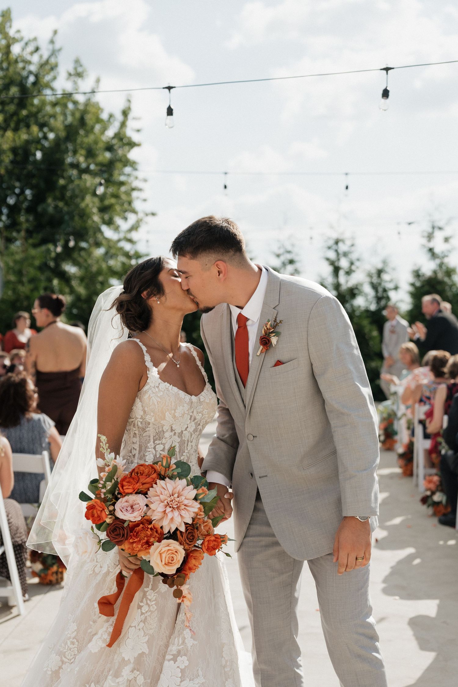 A romantic wedding ceremony outdoors with a couple sharing intimate moments while holding coral and peach floral bouquets.