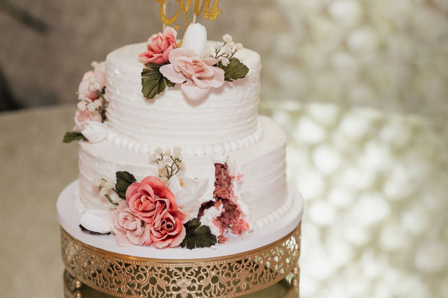Elegant white wedding cake decorated with delicate pink roses on a gold stand.