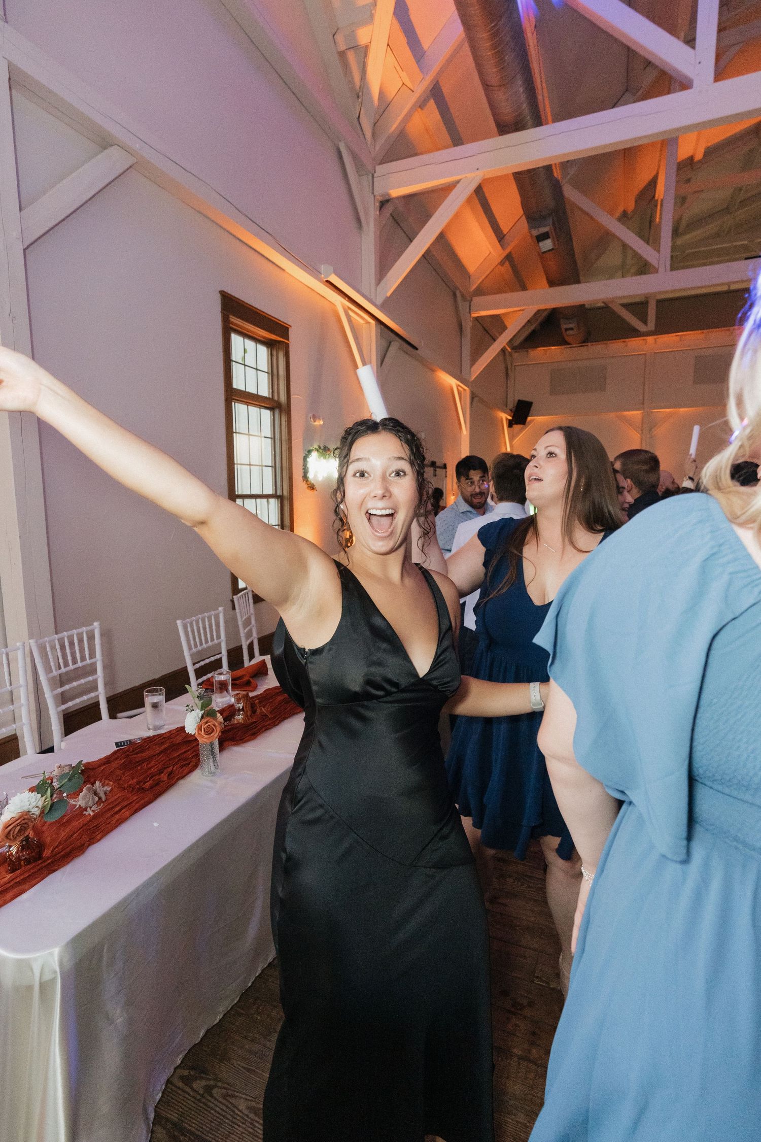 Wedding guests dancing and celebrating with raised arms in venue with vaulted ceilings.