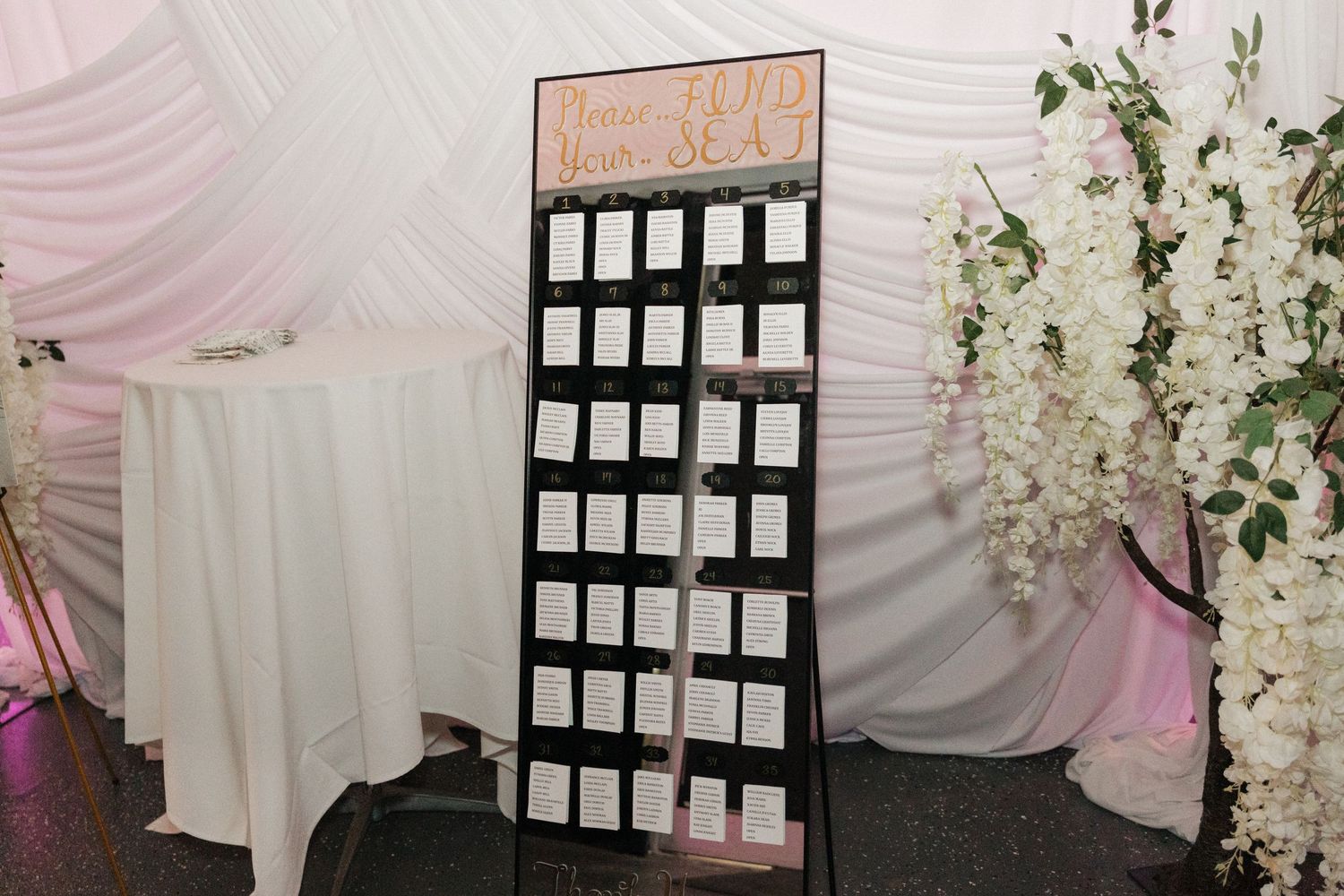 Wedding reception seating chart display with pink draping and floral decorations.
