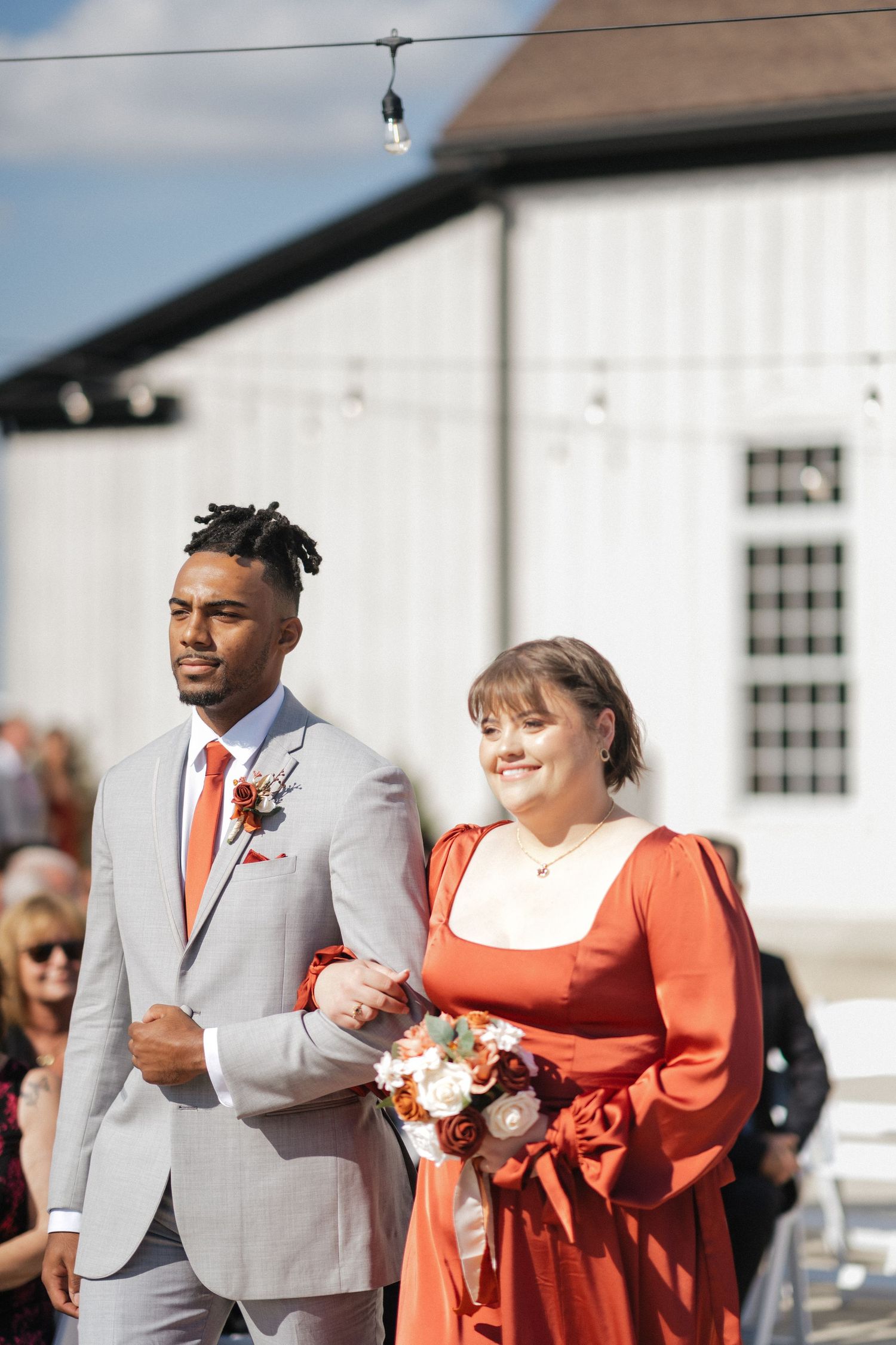 Wedding party members in gray suits and coral dresses walk together outdoors.