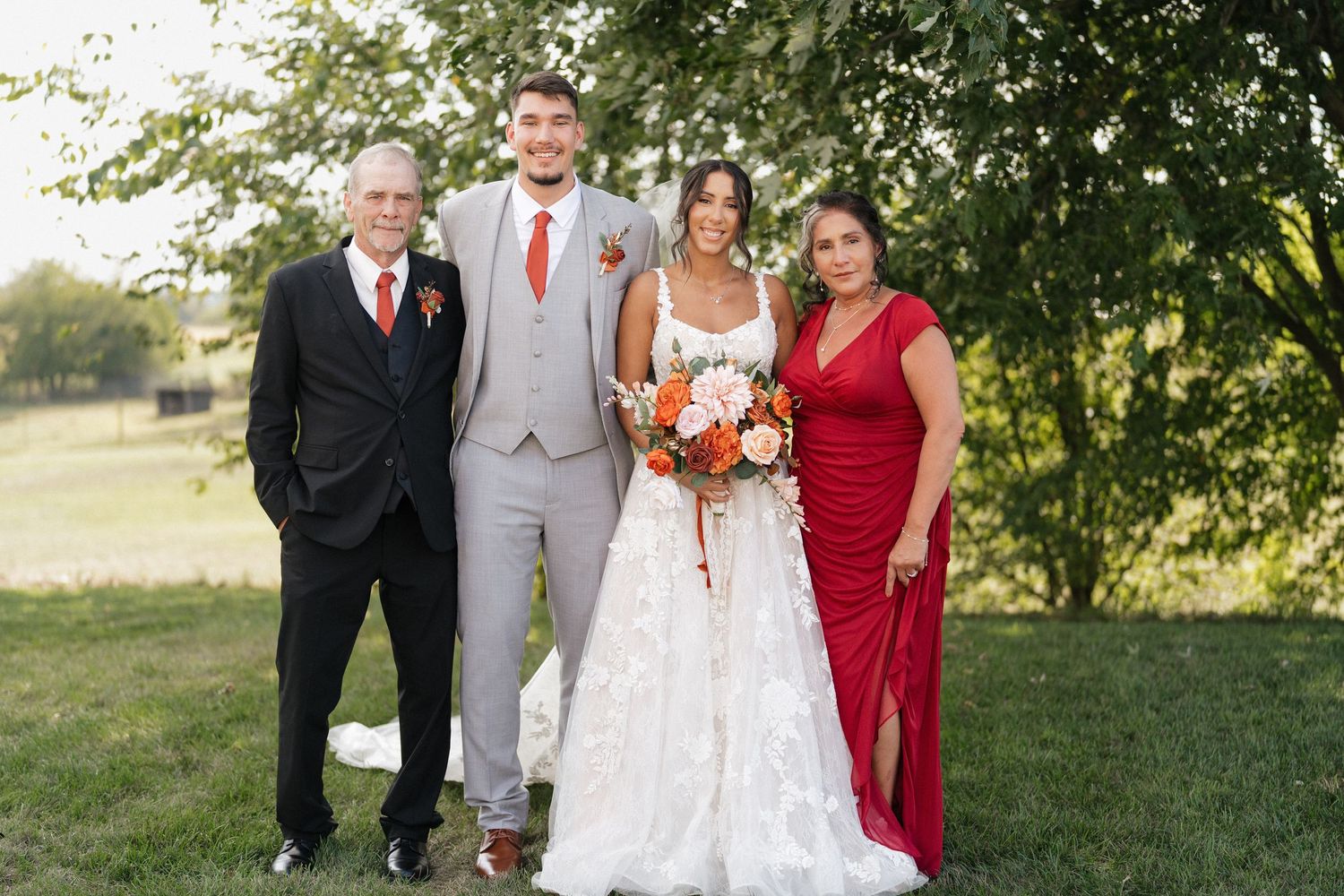 Wedding party poses together outdoors with bridesmaids in red dresses and groomsmen in gray suits.