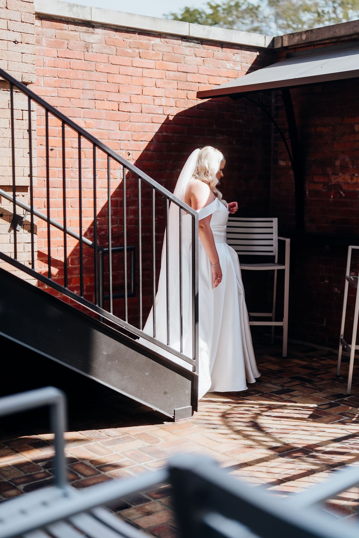 Wedding couple embraces on a brick patio with dramatic shadows and railings.