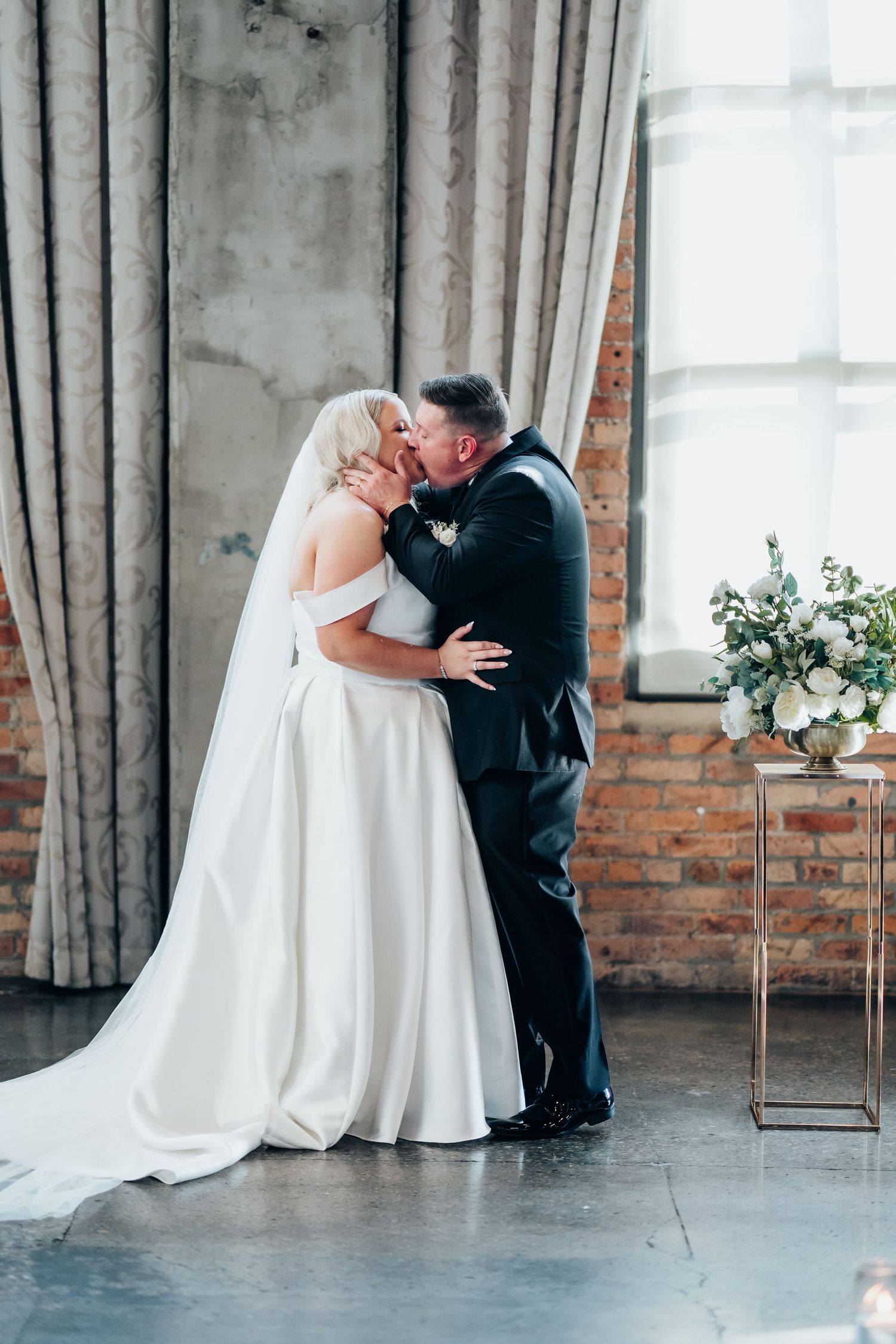 Intimate wedding moment captured in an industrial venue with exposed brick walls and flowing curtains.