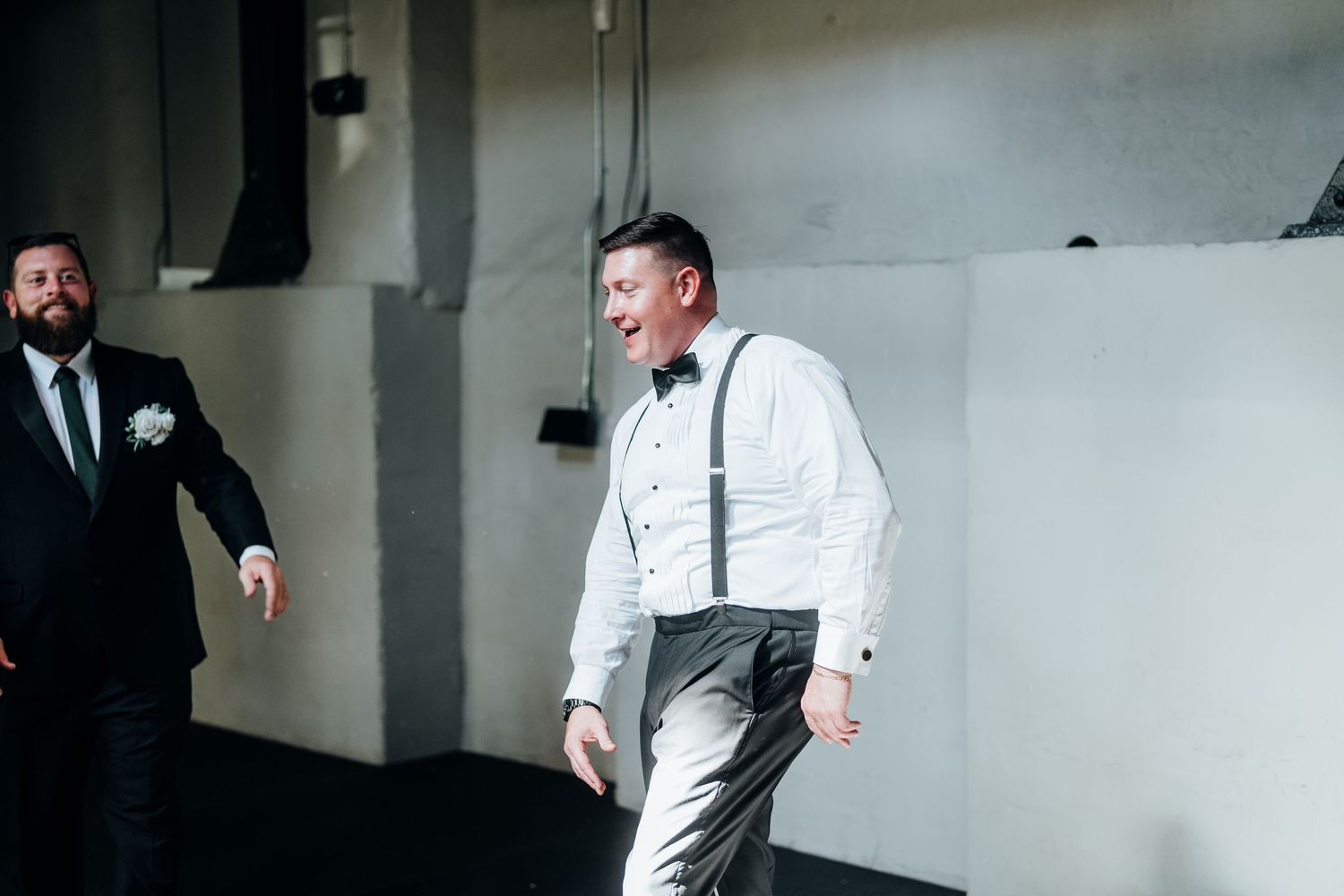 Wedding party members in formal attire preparing in a minimalist room with gray walls.