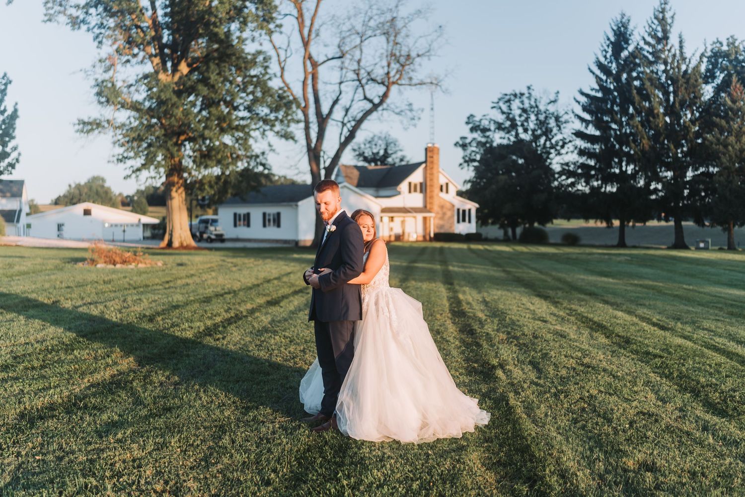 A wedding couple poses in a grassy field at sunset creating romantic silhouettes against the golden sky.