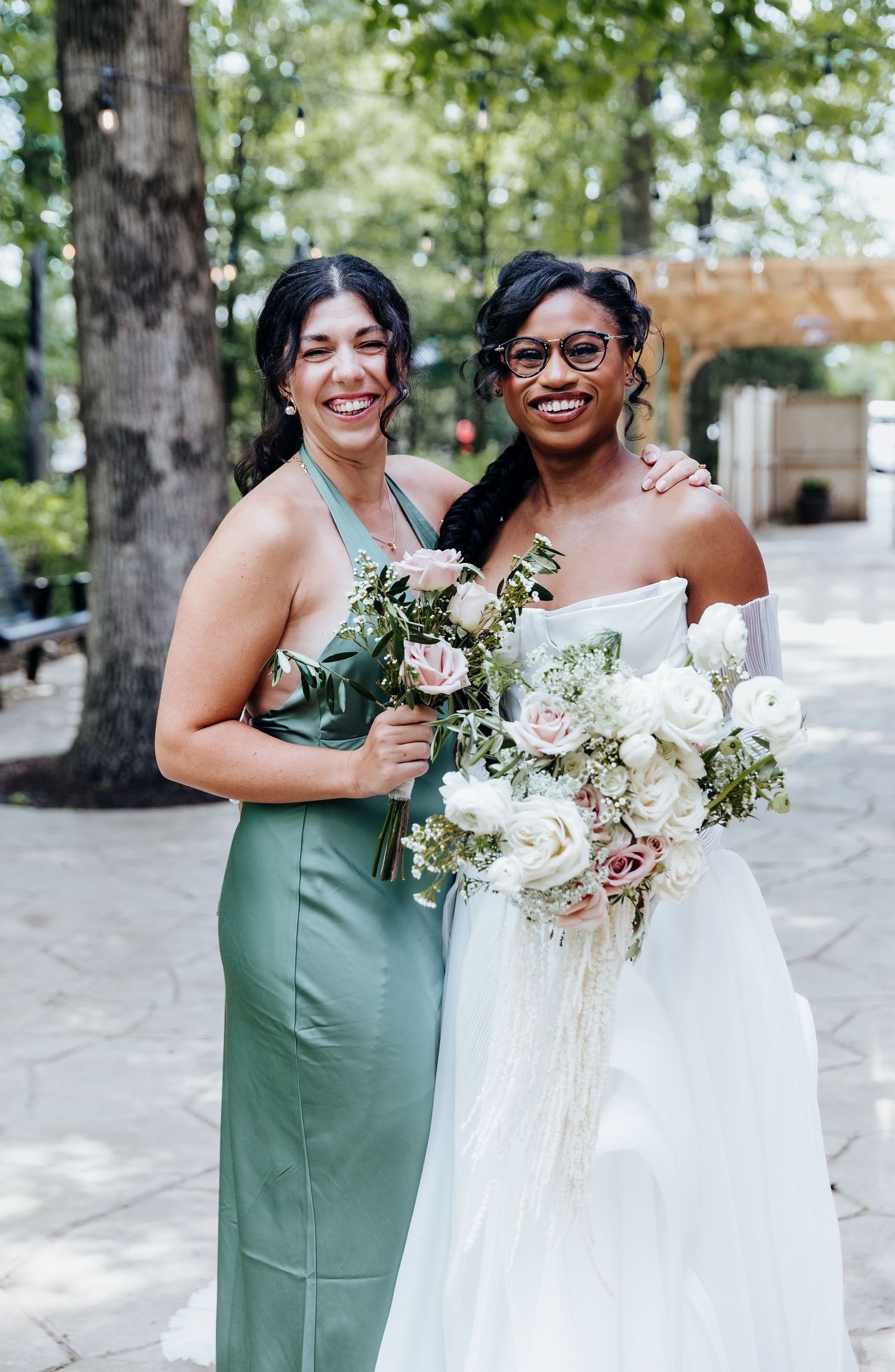 Bridesmaids in sage green dresses pose with bouquets outdoors.