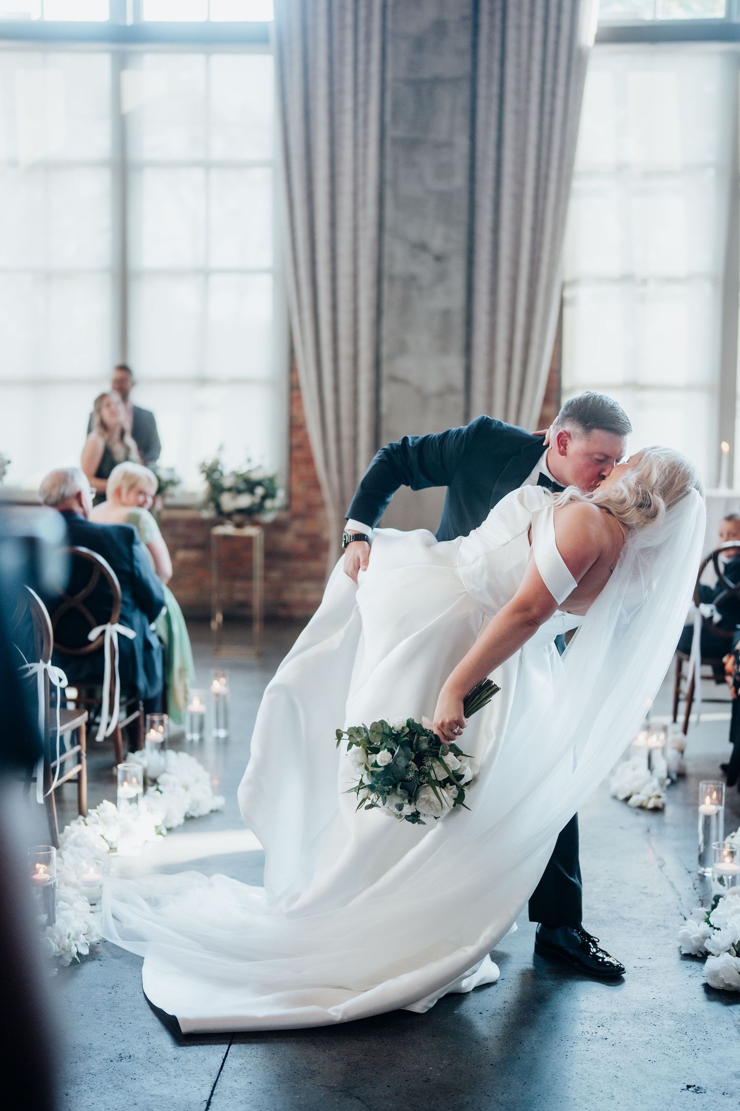 A dramatic dip pose sequence during a wedding photoshoot in a bright industrial venue.