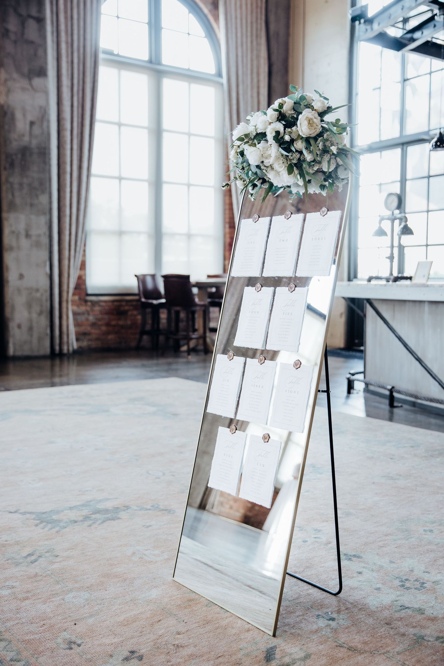 A wedding seating chart display with white boards and floral arrangements in an industrial-style venue.